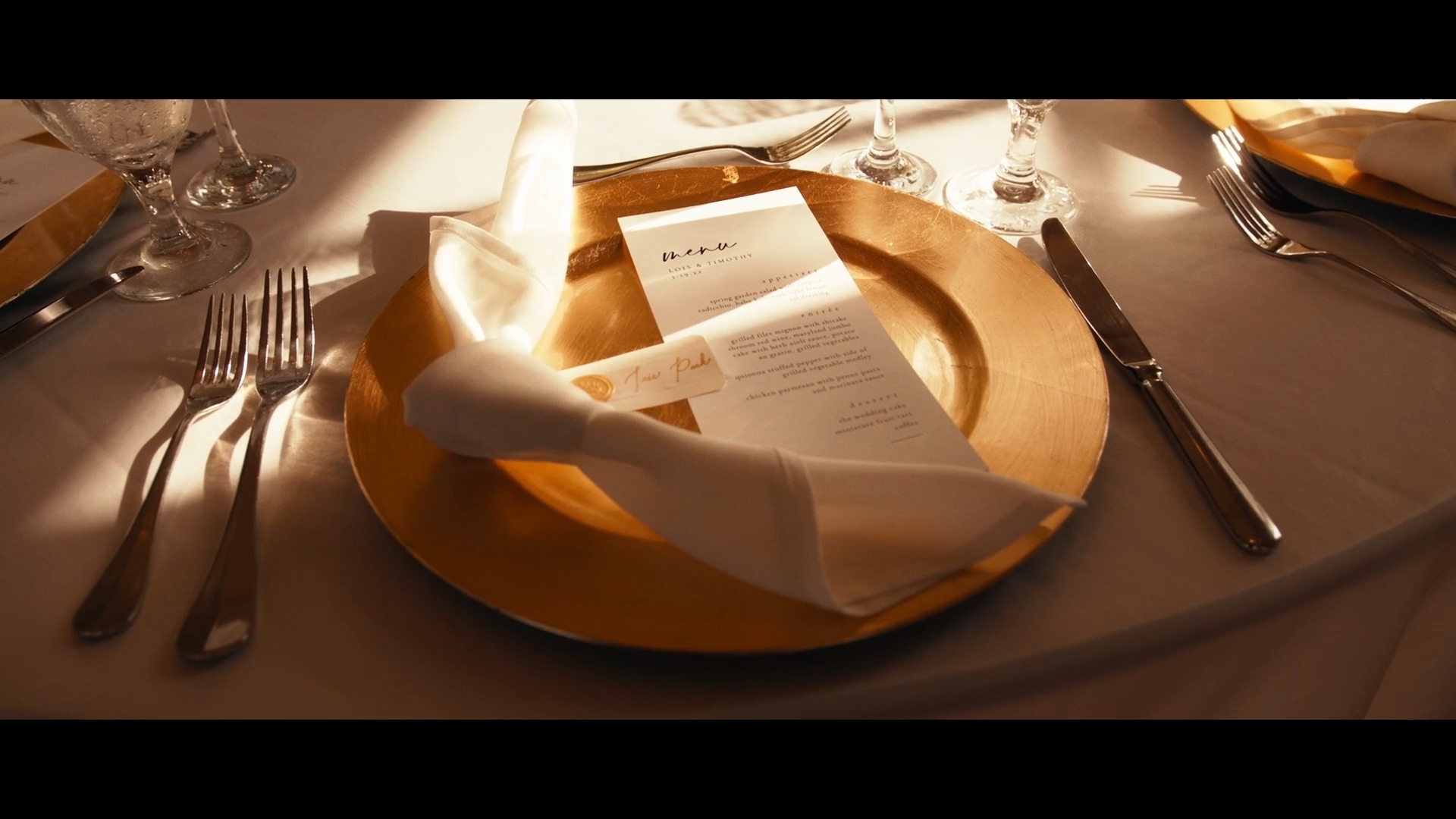 Elegant table setting with a gold charger plate, white napkin, and silverware, with a menu on the plate.