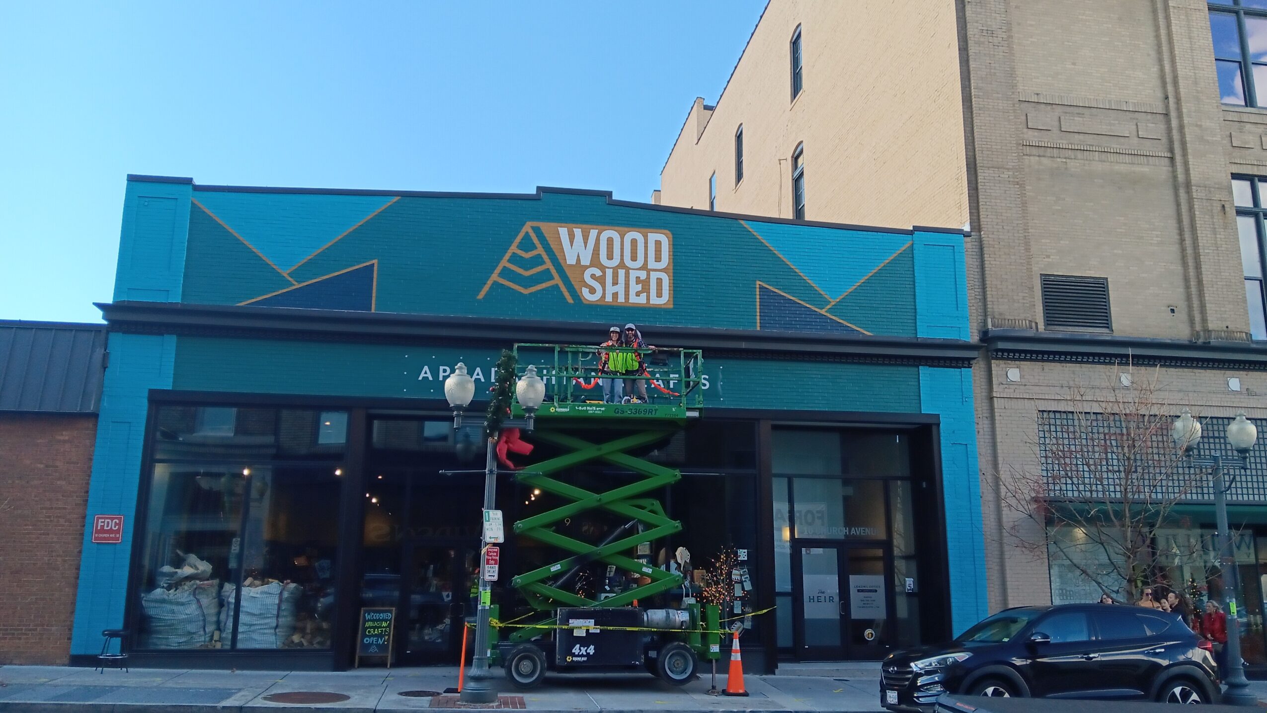 Storefront with blue facade and sign reading 'Wood Shed', large glass windows, and a small lift in front.