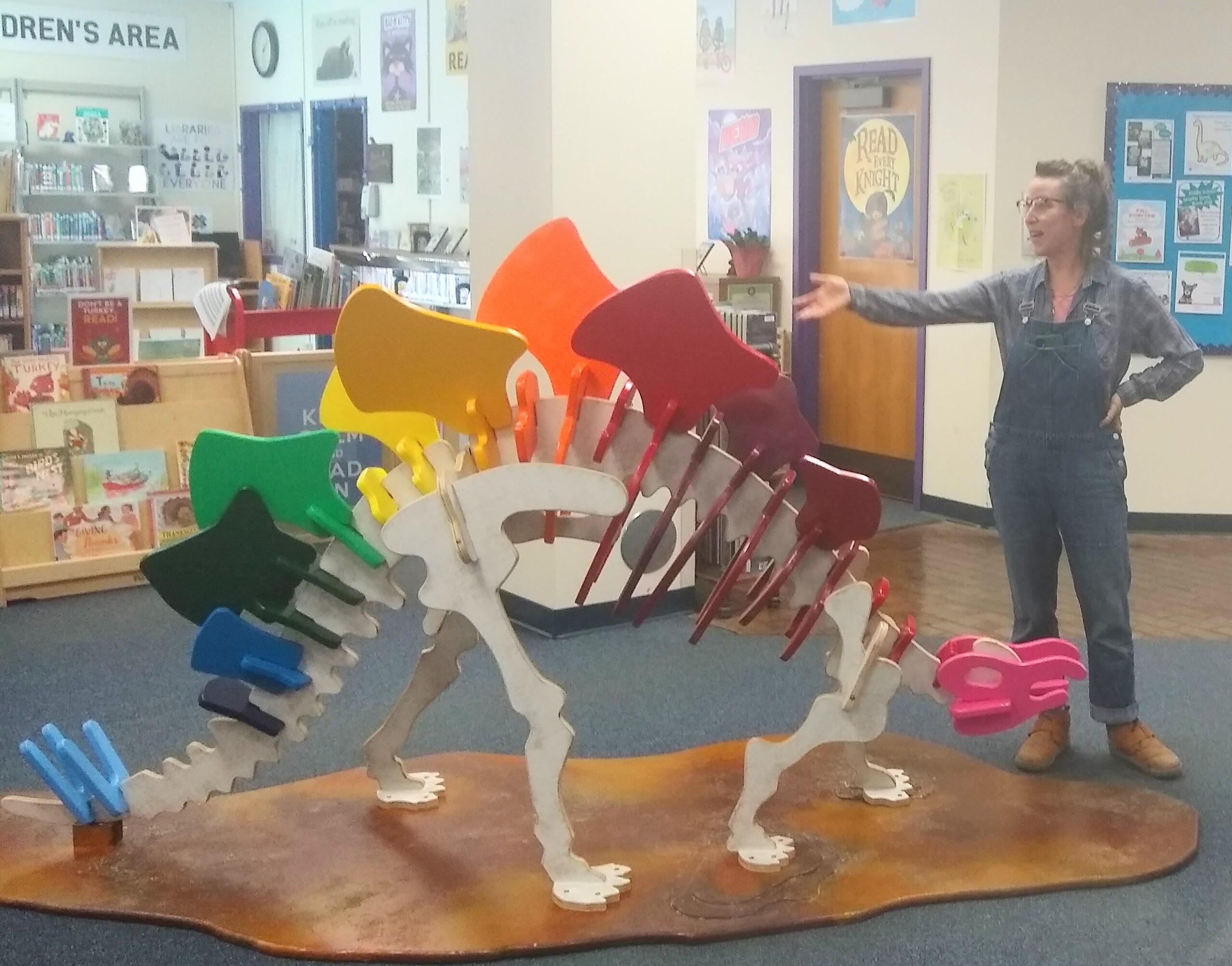 Woman pointing at colorful dinosaur sculpture in a children's area of a library or bookstore.