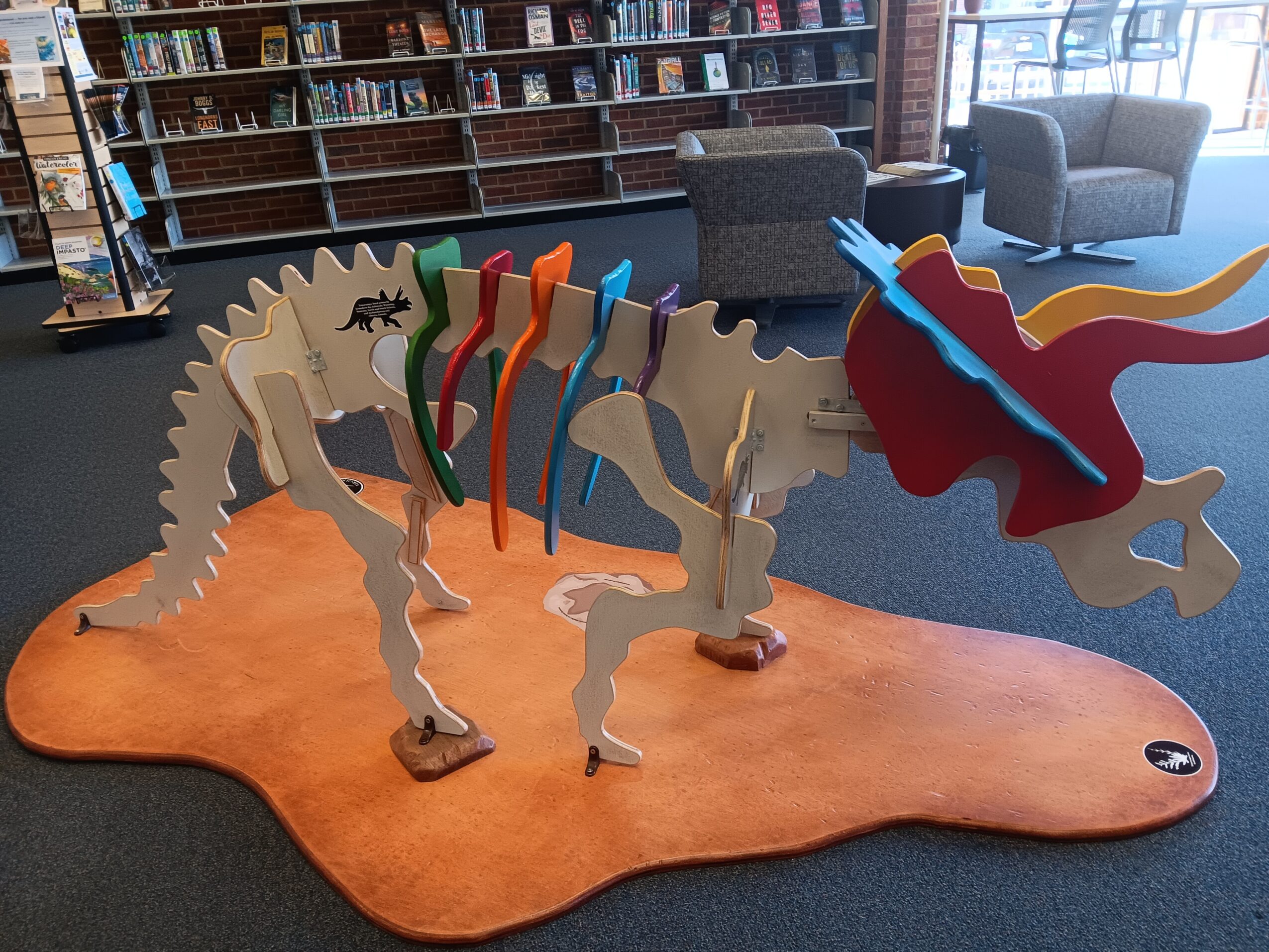 Colorful dragon sculpture with multiple legs and a long body, displayed on an orange platform inside a library or bookstore.