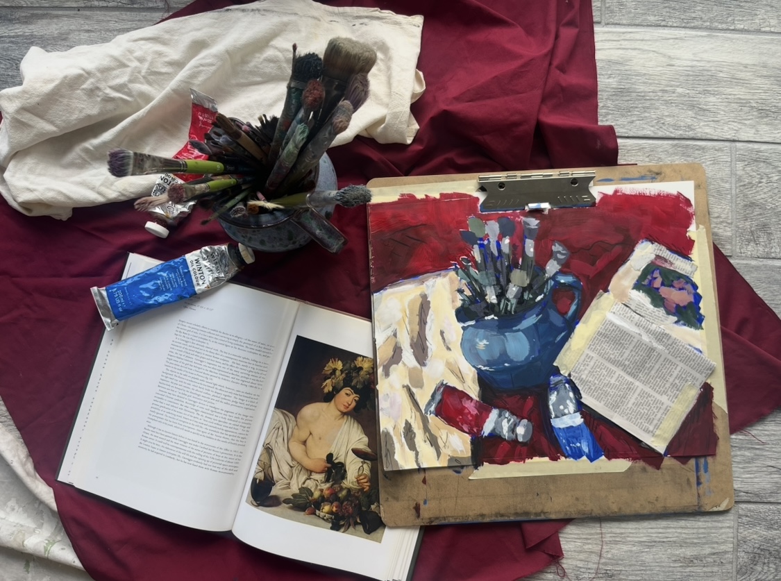 Paintings, books, and art supplies on a red cloth, with a tube of paint and a canvas featuring a still life of flowers.