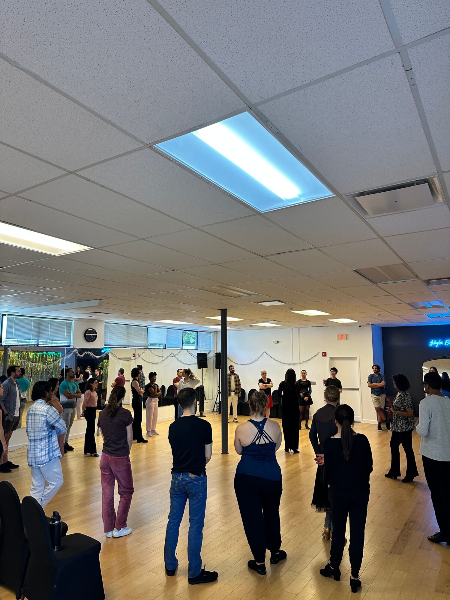 People standing and walking in a brightly lit indoor space with a wooden floor and large windows.