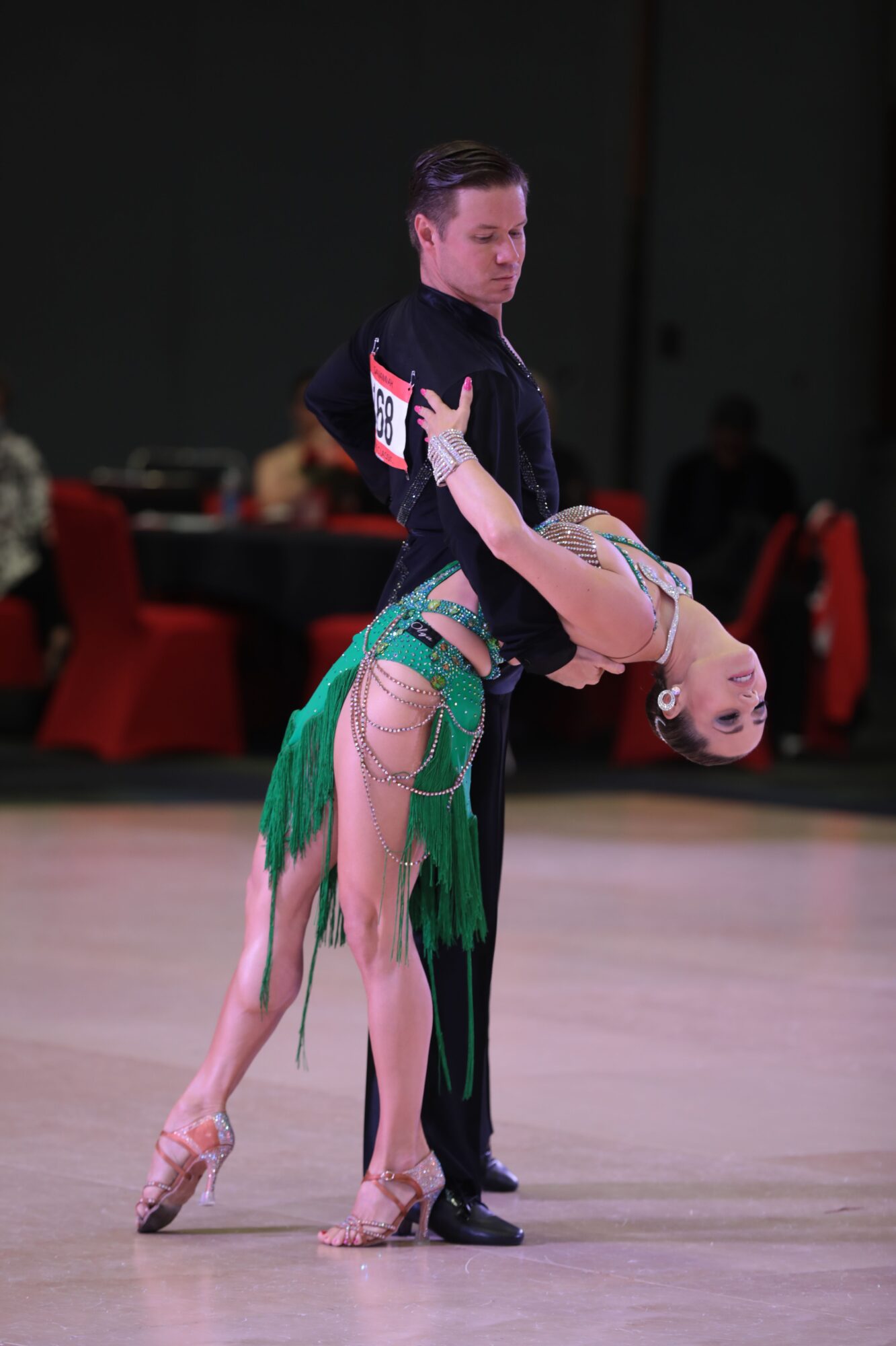 Two dancers perform on stage, one in a green costume and the other in a black outfit, with a dark background.
