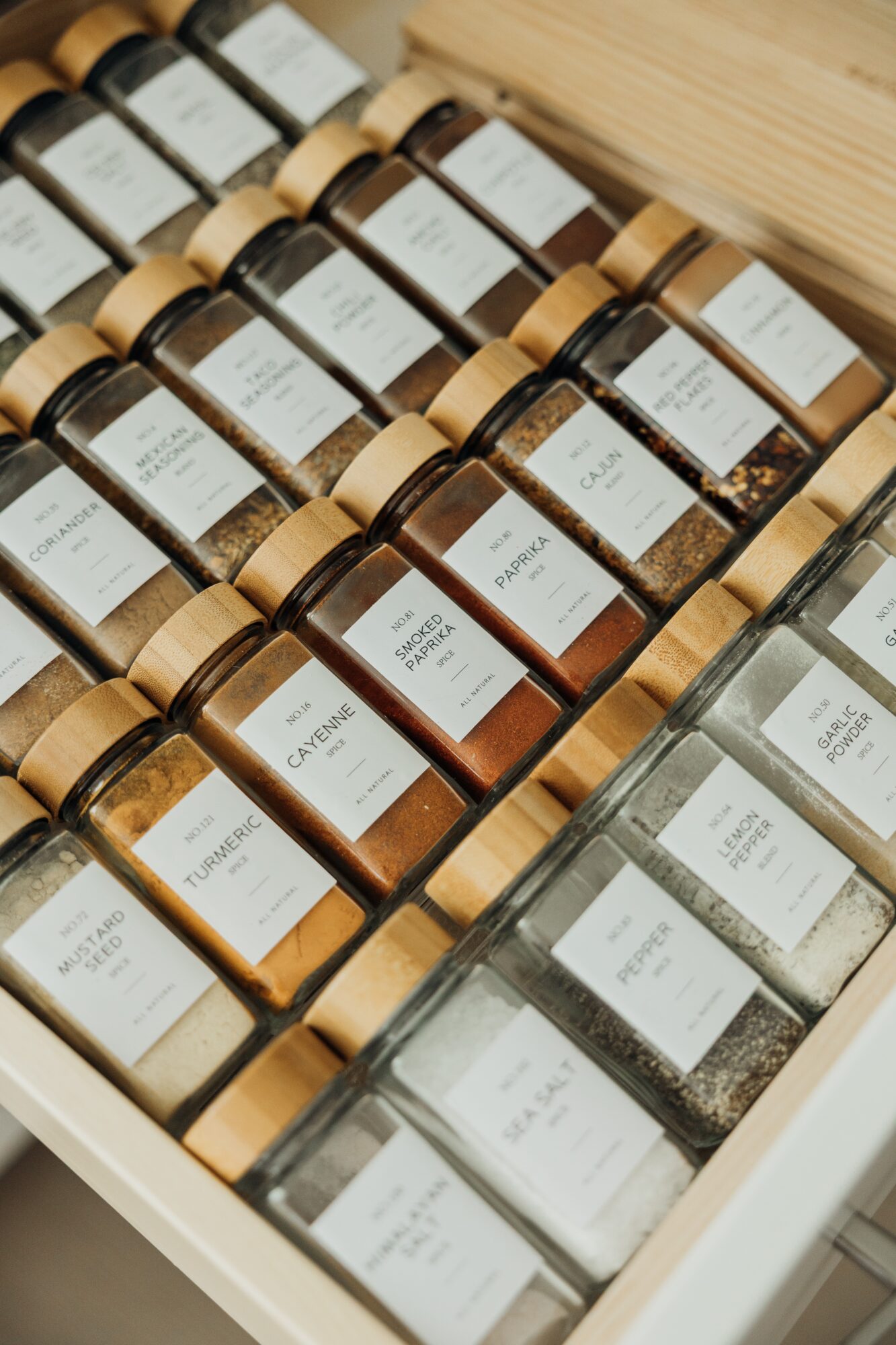Multiple jars with labels arranged in a wooden box, containing spices or herbs, viewed from above.