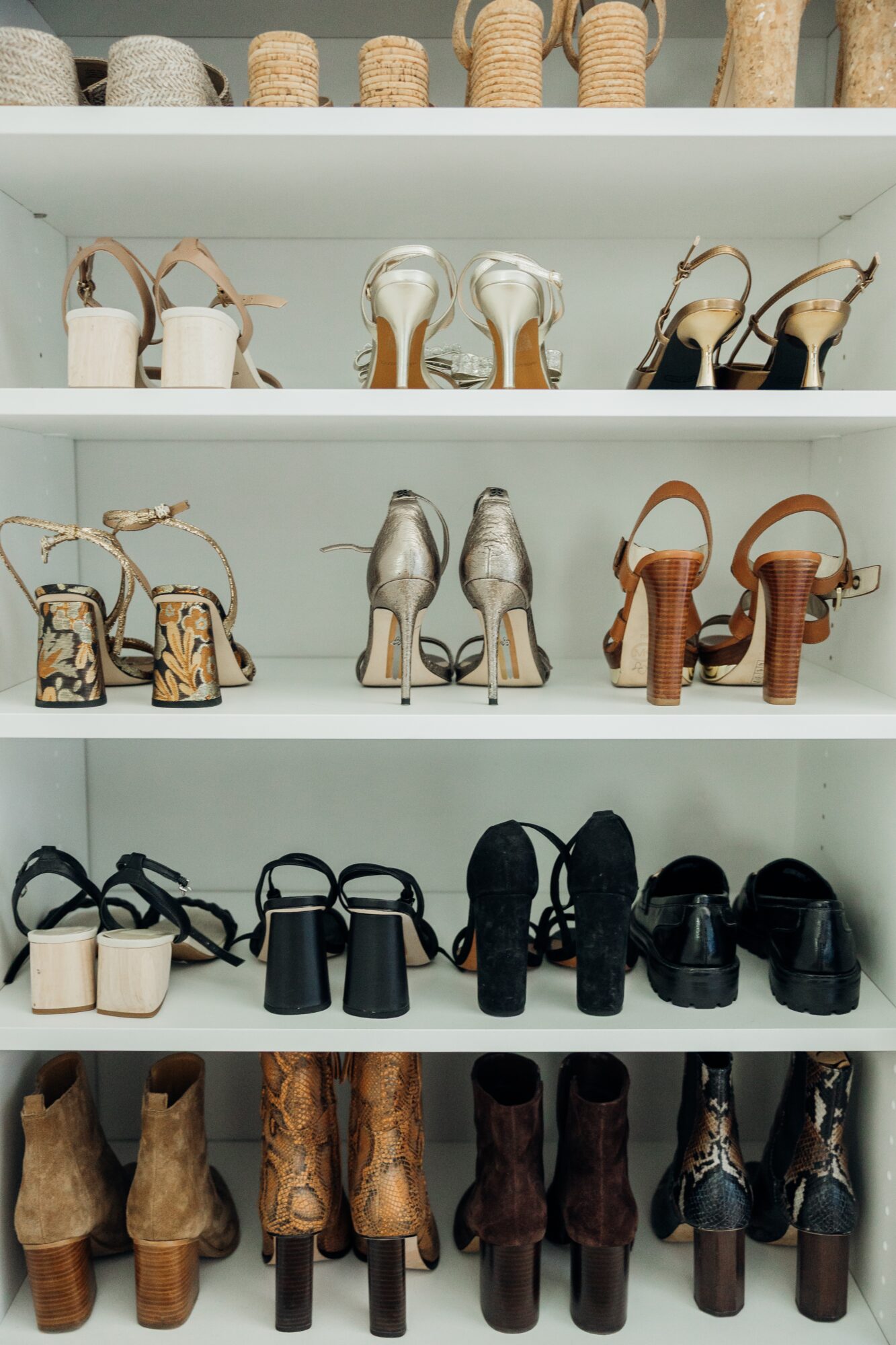 Display of various high-heeled shoes on white shelves, arranged by style and color, with a variety of heel heights and designs.