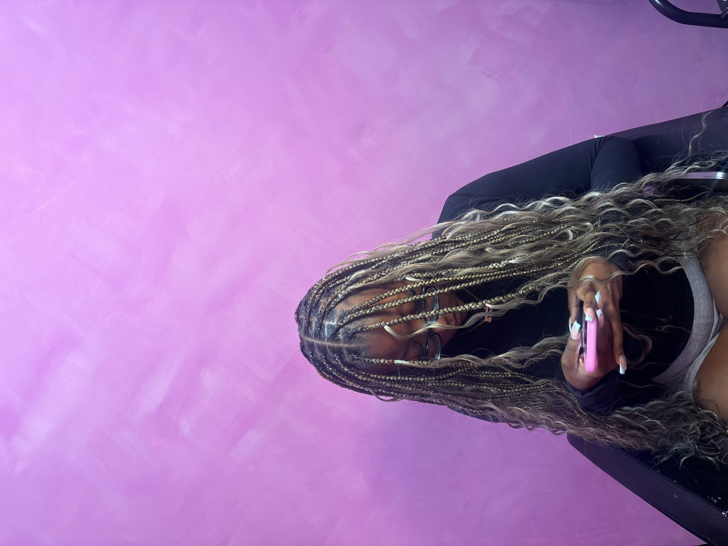 Person with long, braided hair taking a selfie in a room with pink and purple walls.