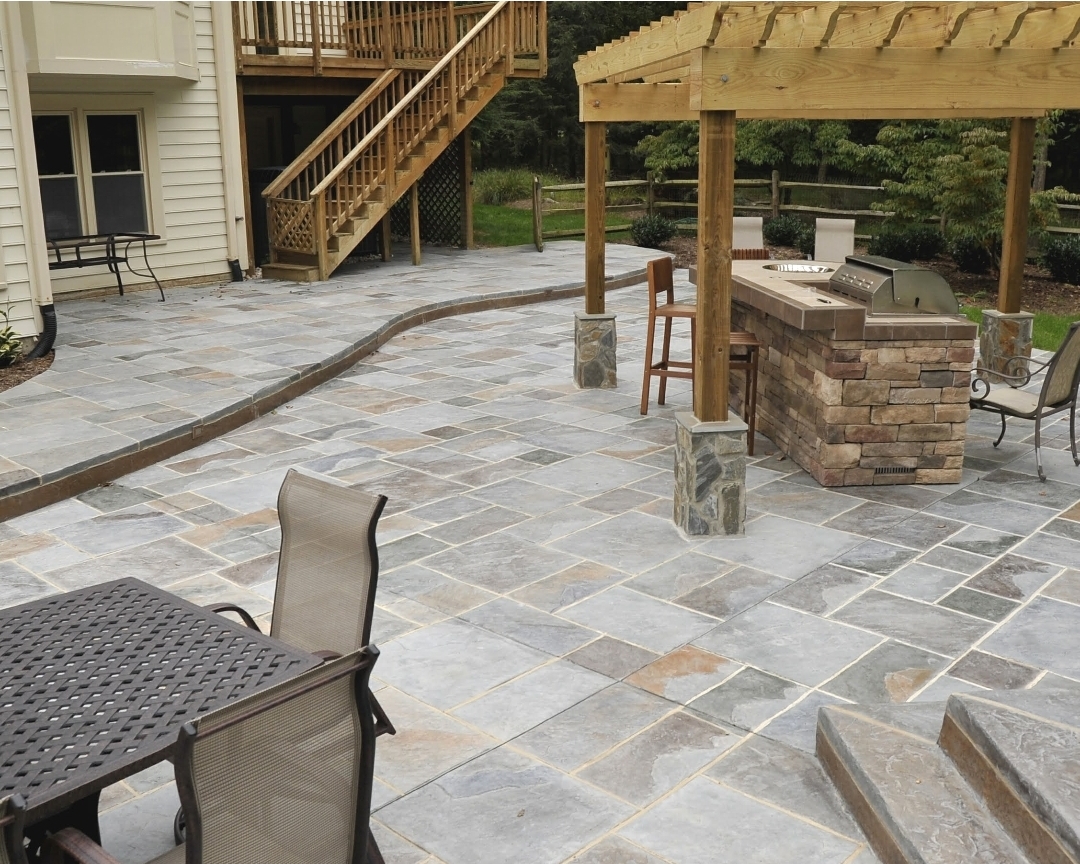Outdoor patio with stone flooring, a wooden pergola, and outdoor furniture including chairs and a table.