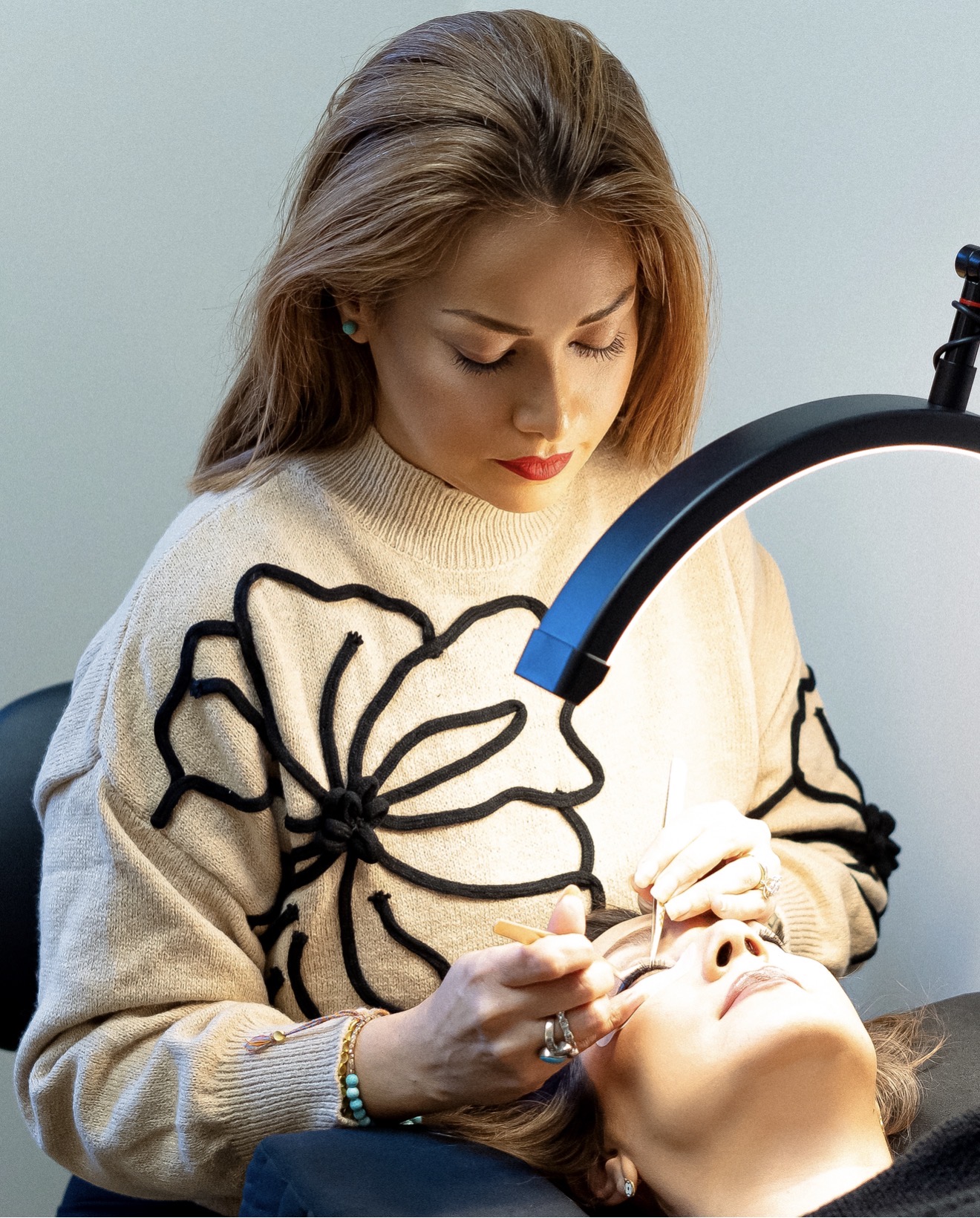Woman performing a procedure on a person's eye with a specialized lamp, wearing a cream sweater with black floral design.