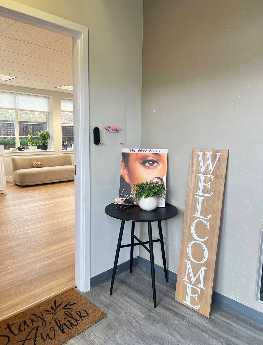 Corner of a room with a black round table, a welcome sign, and a picture of a woman's eye on the wall.