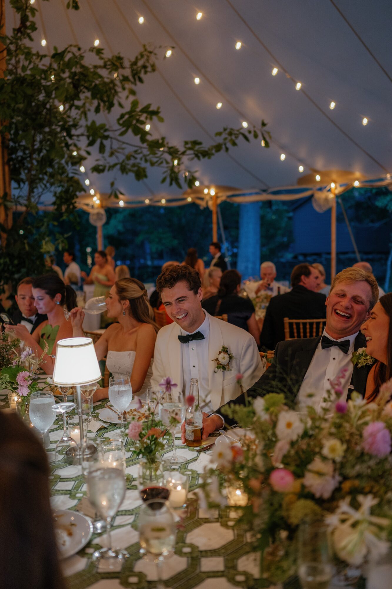 People seated at a decorated banquet table under string lights during evening, smiling and enjoying the event.