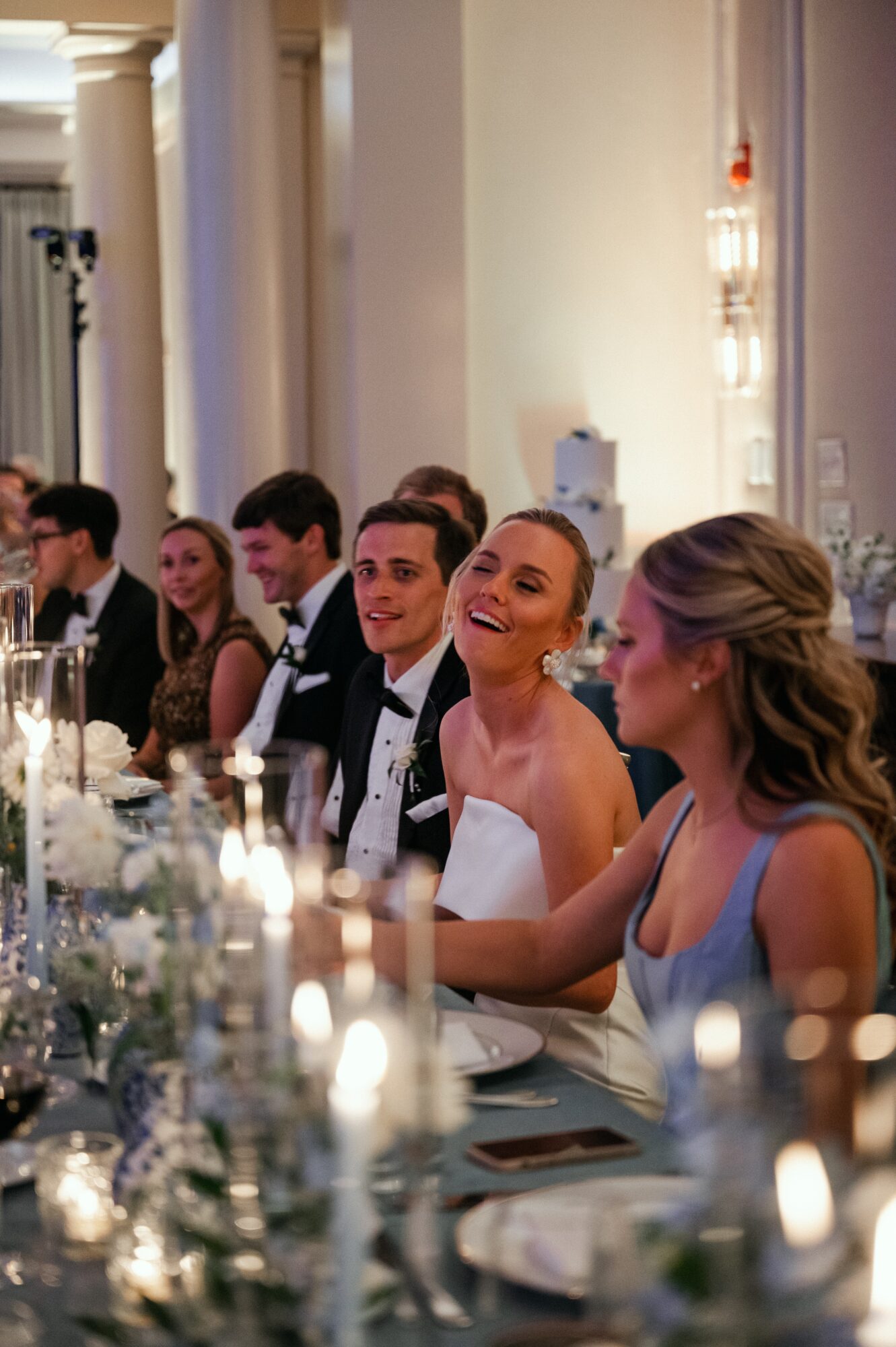 People seated at a formal dinner table, smiling and engaging, with elegant decor and candles, in a grand room.