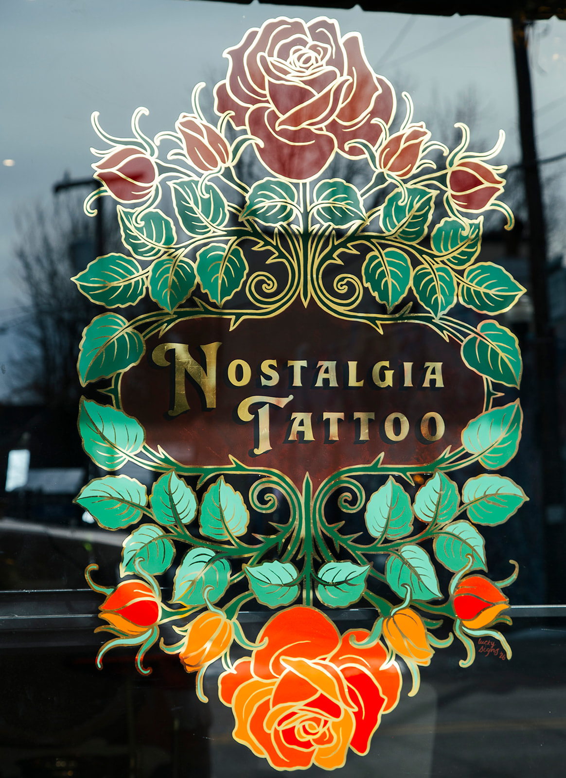 Decorative floral design with roses and leaves, and text reading 'Nostalgia Tattoo' in gold, on a dark background.