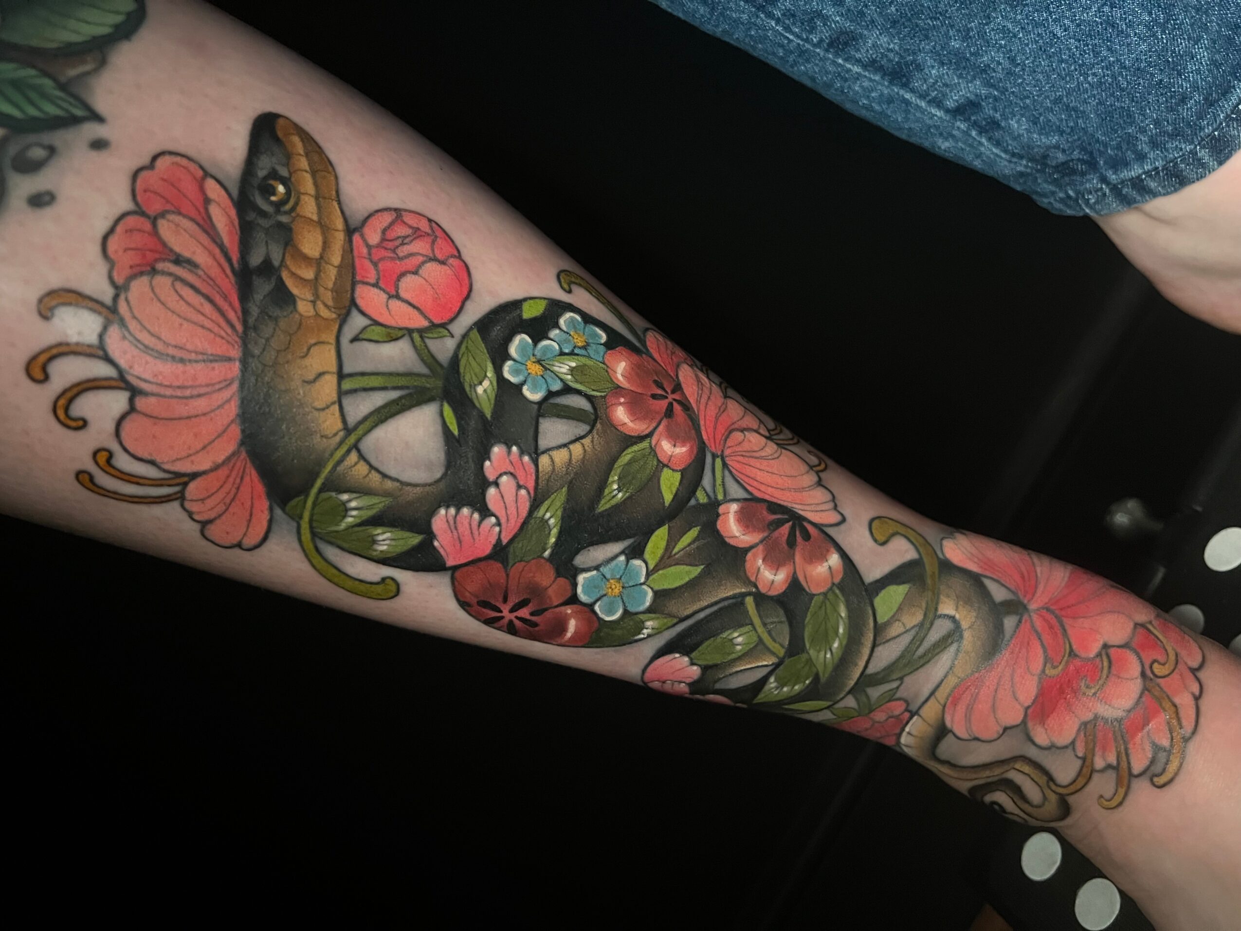 Tattoo of a snake intertwined with pink and blue flowers on a person's arm.