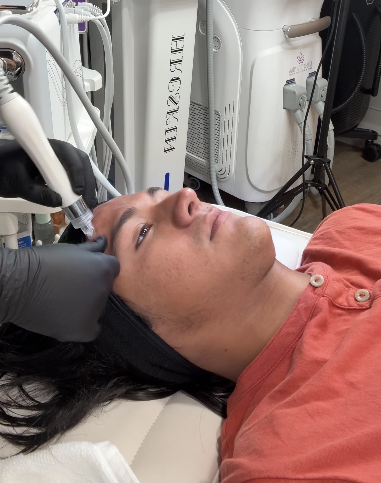 Person lying on medical bed receiving facial treatment with equipment nearby.
