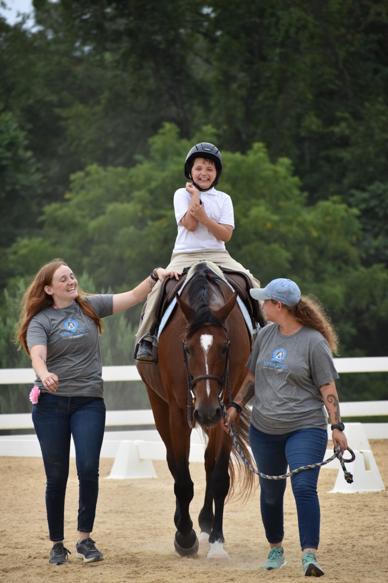 Three people and a horse outdoors with trees in the background, two women and a girl, one woman petting the horse.