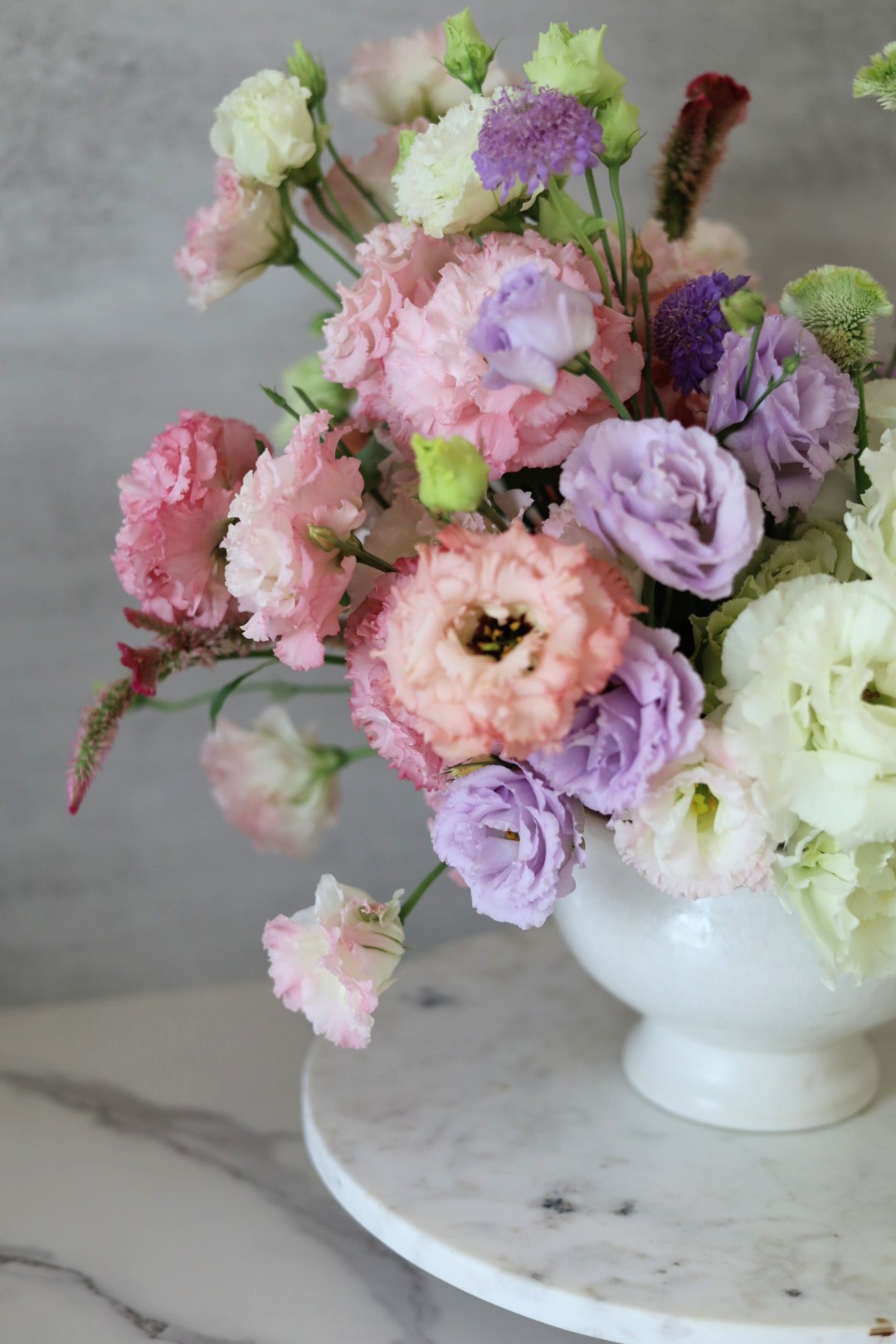 Bouquet of pink, purple, and white flowers in a white vase on a marble surface.