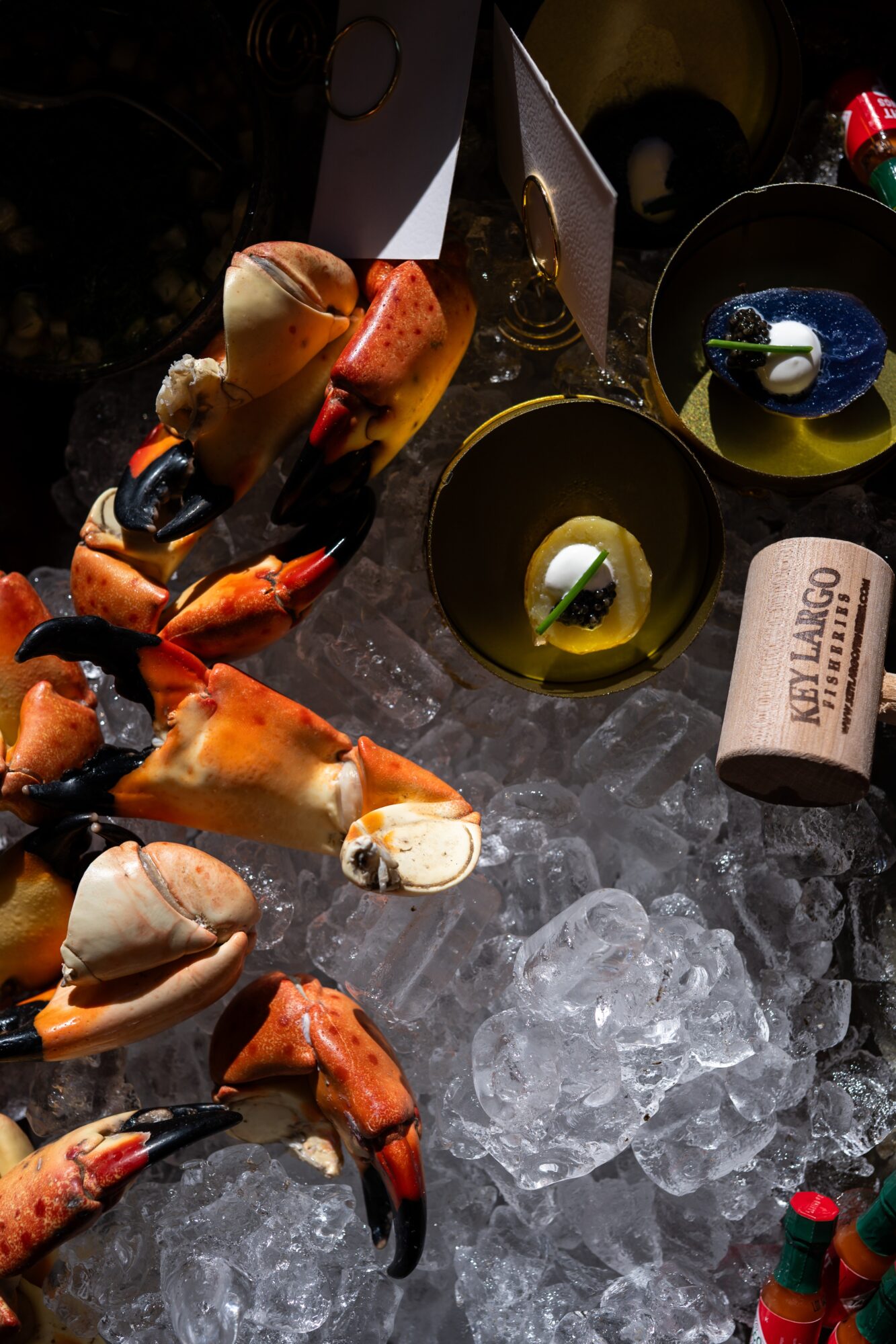 Seafood dishes, bowls, and ice on a dark surface, with a wine glass and a paper roll visible.