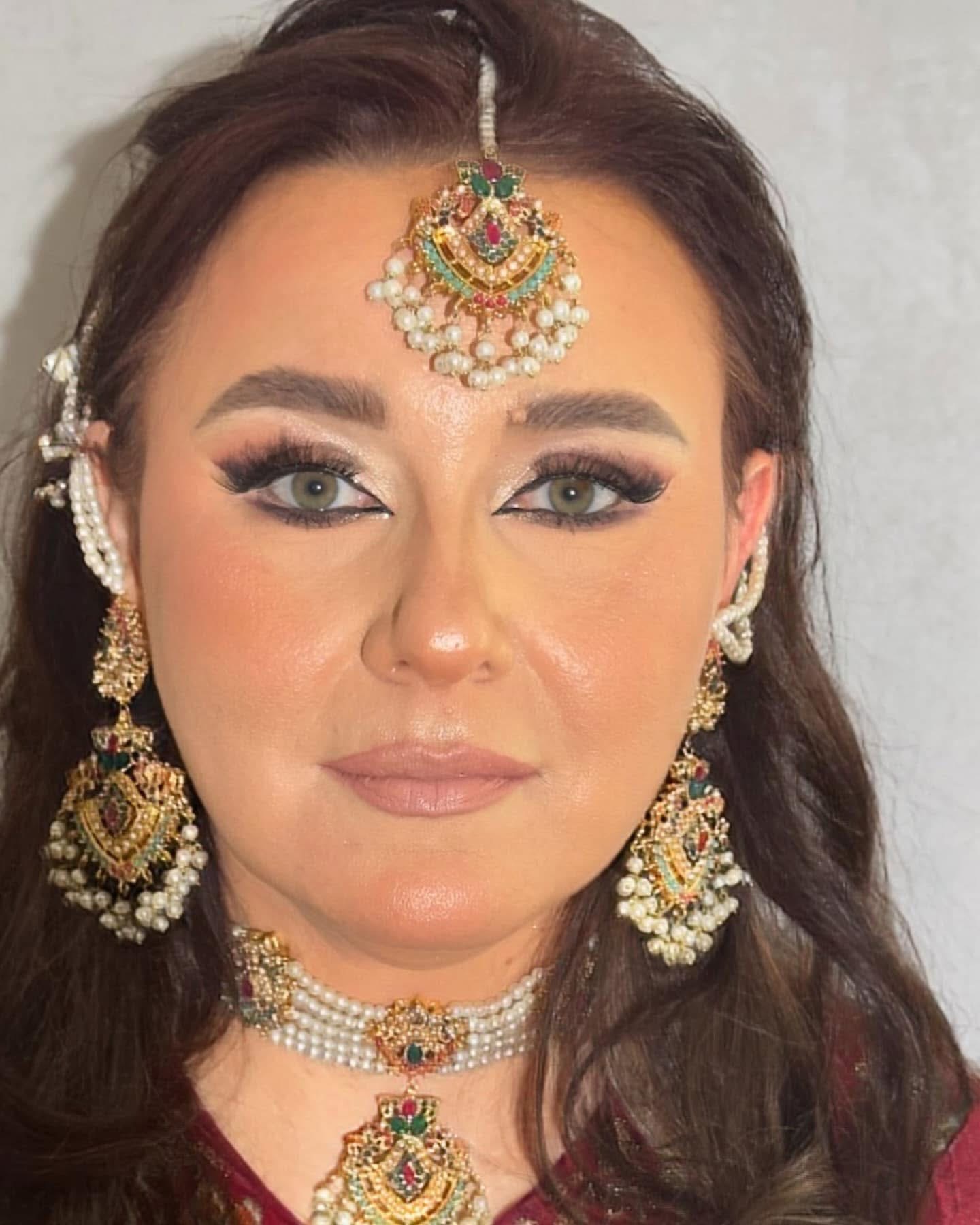Woman wearing traditional jewelry, including earrings, necklace, and forehead ornament, with makeup and dark hair.