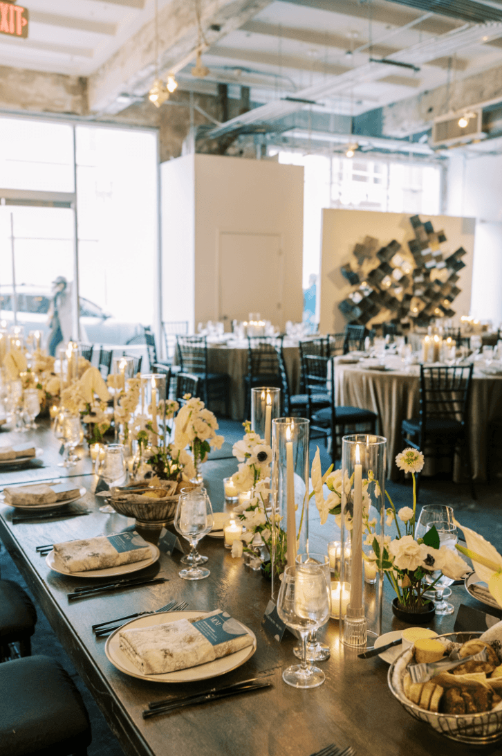 Elegant banquet table with floral centerpieces, candles, and place settings in a bright, modern event space.
