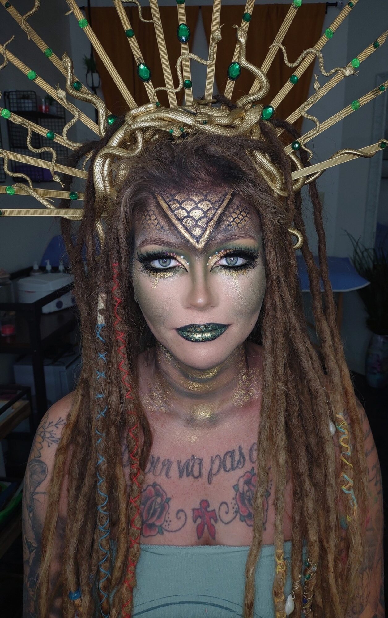 Woman with elaborate gold headpiece and dreadlocks, makeup, and tattoos, looking directly at the camera.