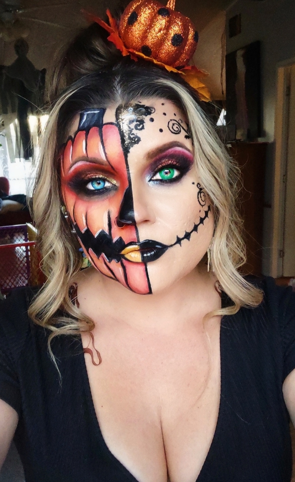 Woman with half Halloween face paint, pumpkin headband, and black top, indoors with blurred background.
