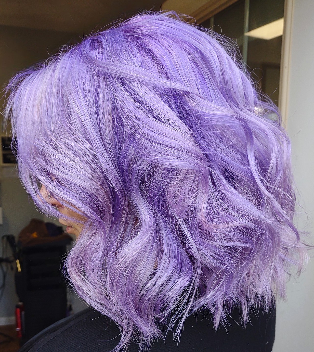 Side view of a person with wavy, shoulder-length lavender hair.