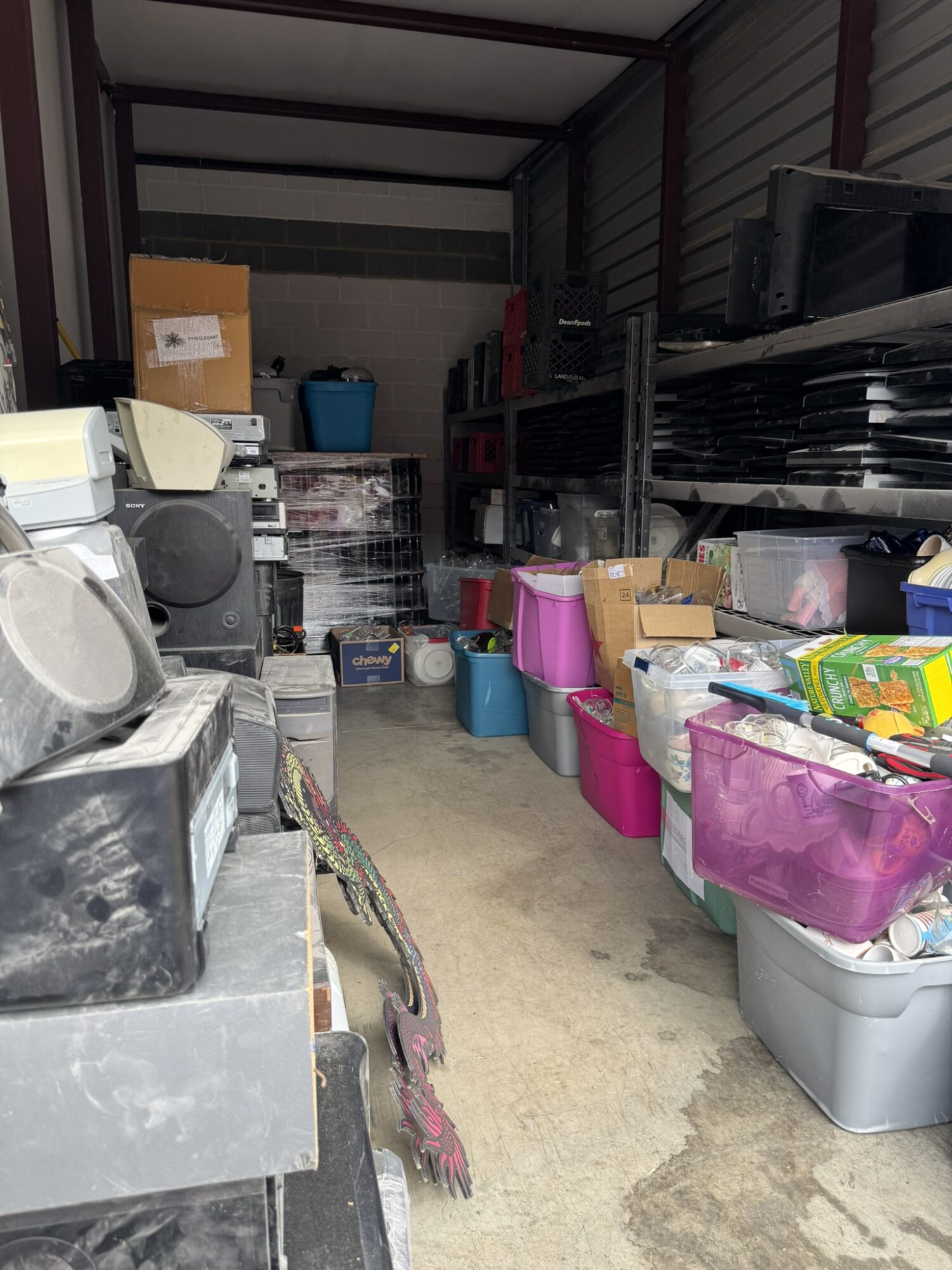 Storage unit with shelves, boxes, and various household items, viewed from the side with a concrete floor.