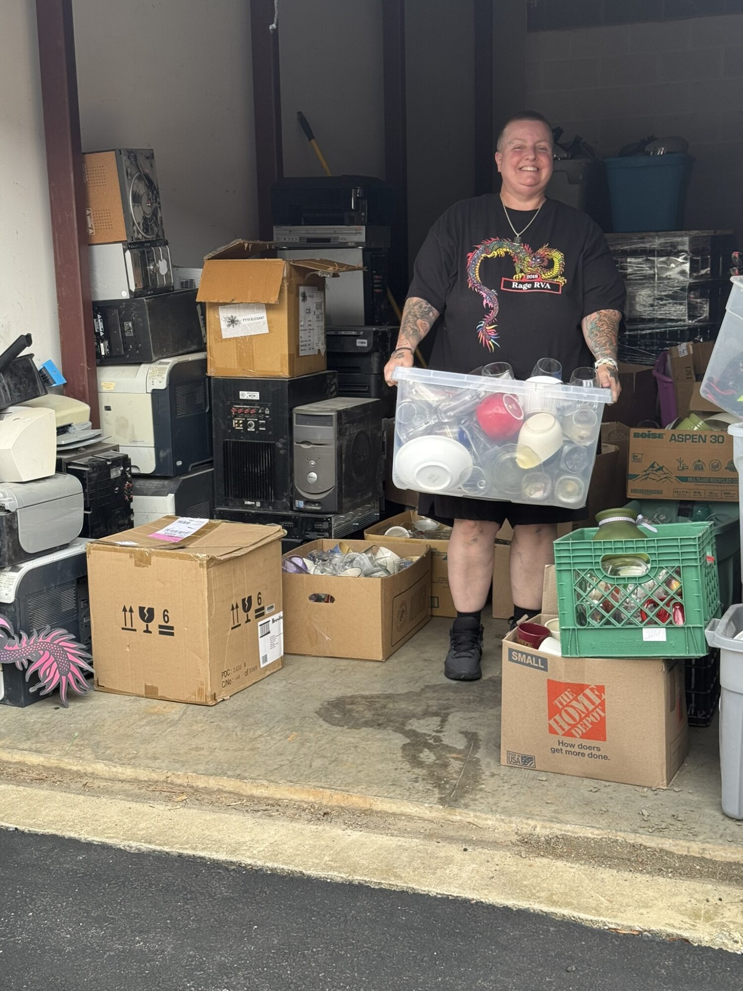 Person holding a clear plastic bin filled with cups and balls, standing in a cluttered storage area, smiling.
