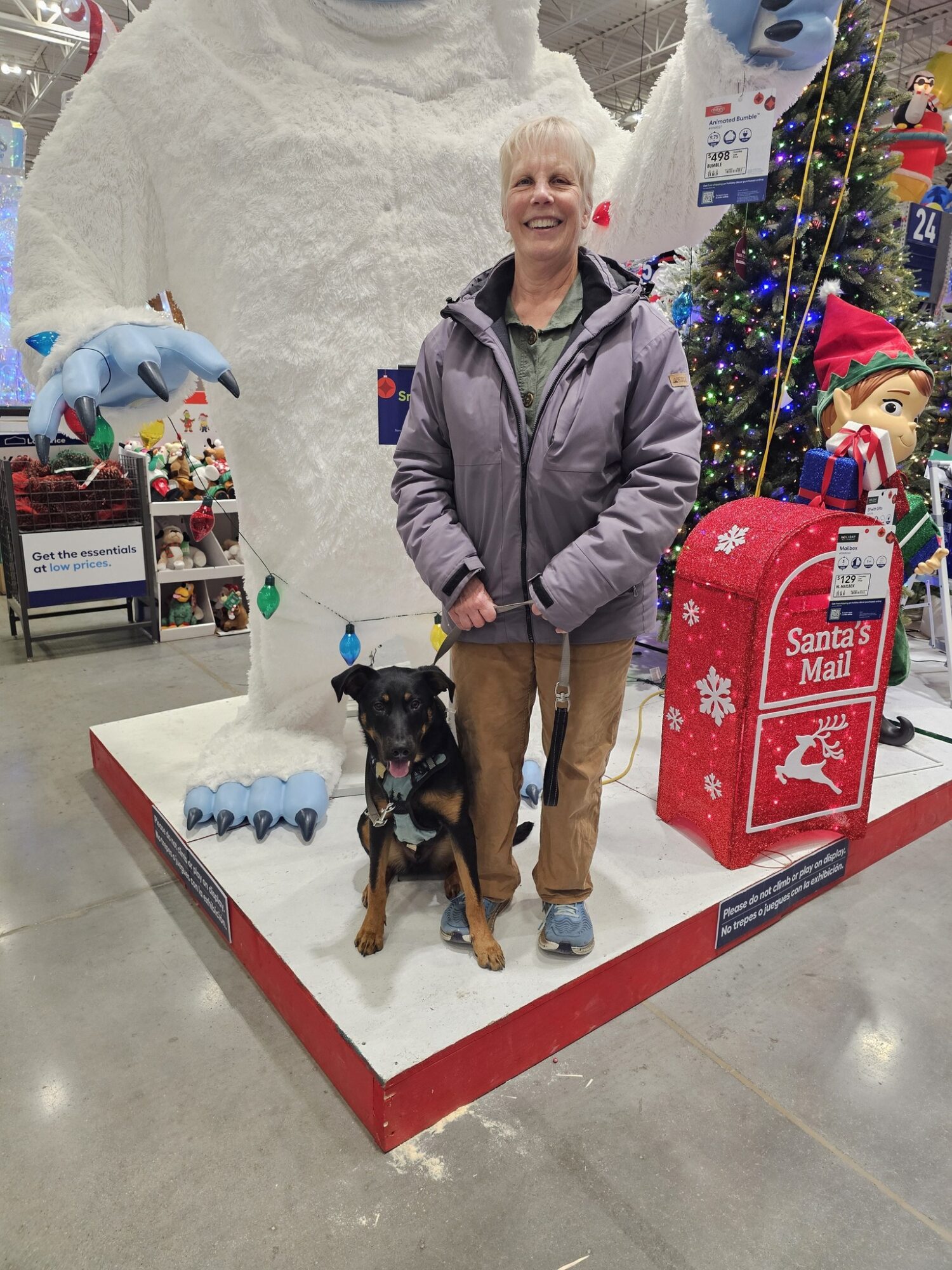 Woman standing with a dog in front of a Christmas display with a snowman figure and holiday decorations.