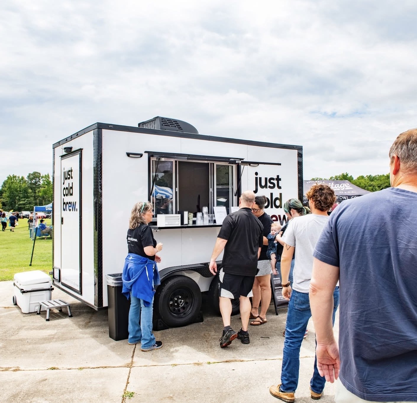 People gather around a mobile food truck outdoors on a cloudy day.