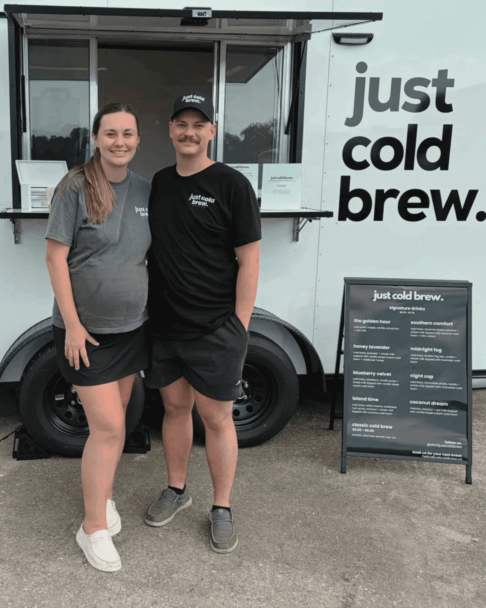 Two people stand in front of a food truck with a sign that says
