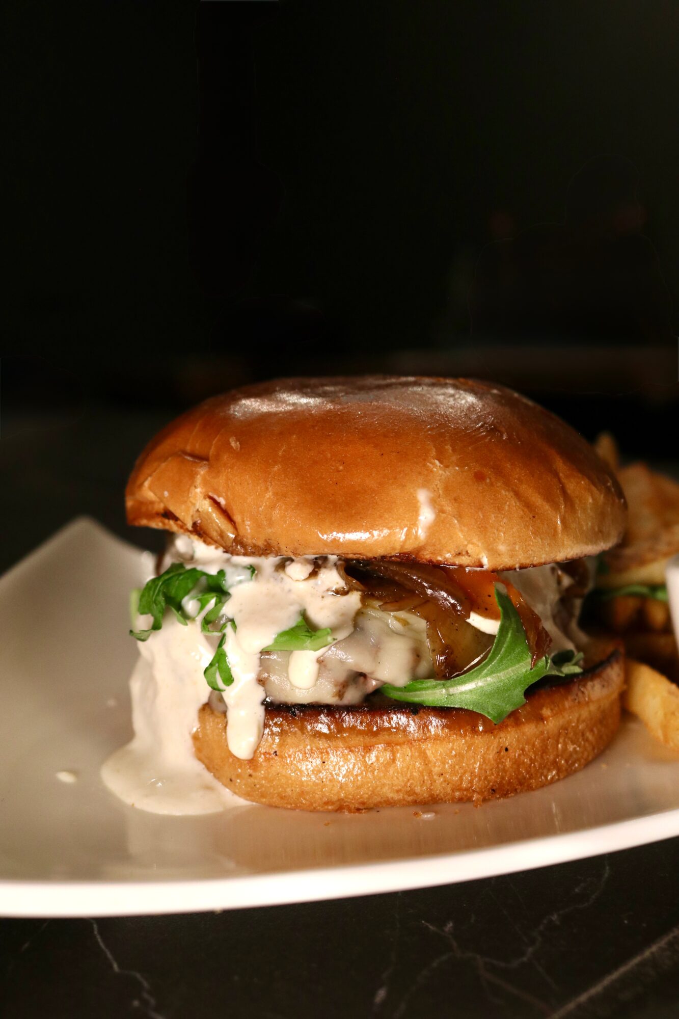 Burger with lettuce, sauce, and a bun on a white plate, with a dark background.