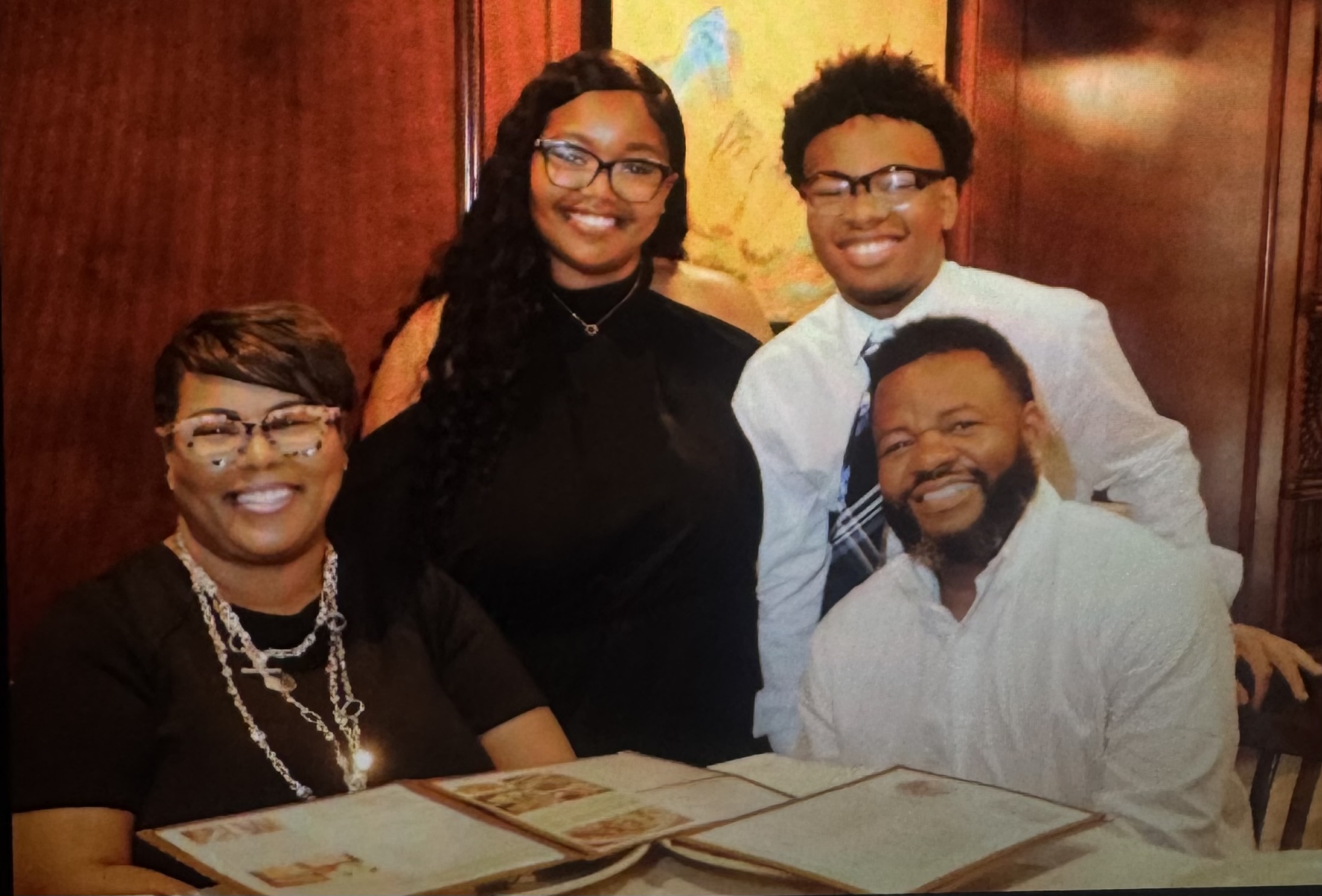 Four people smiling at a table with menus, in a warmly lit room, two women and two men, all wearing glasses.