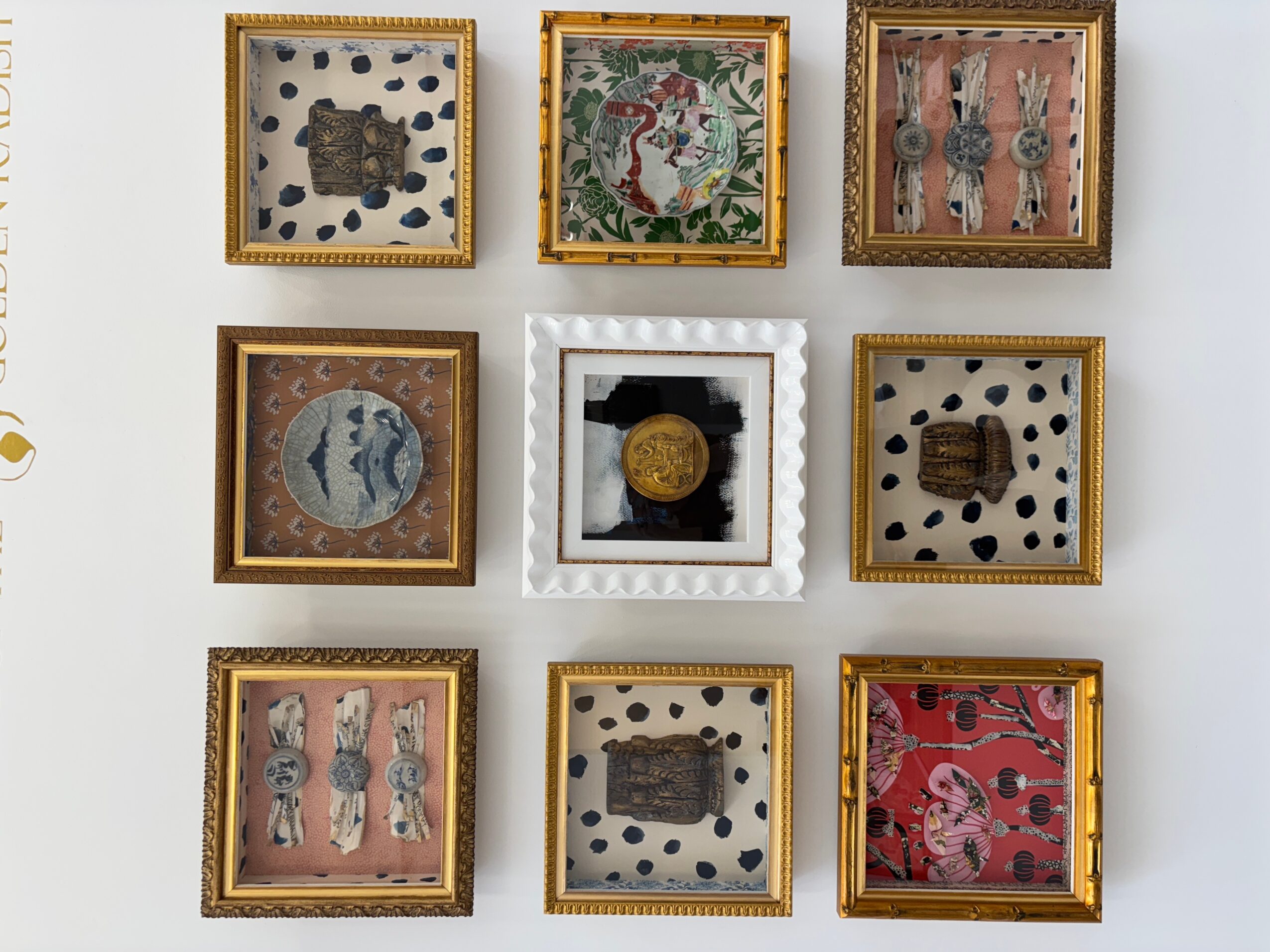 Nine framed artworks arranged in a 3x3 grid on a white wall, with various designs and colors.