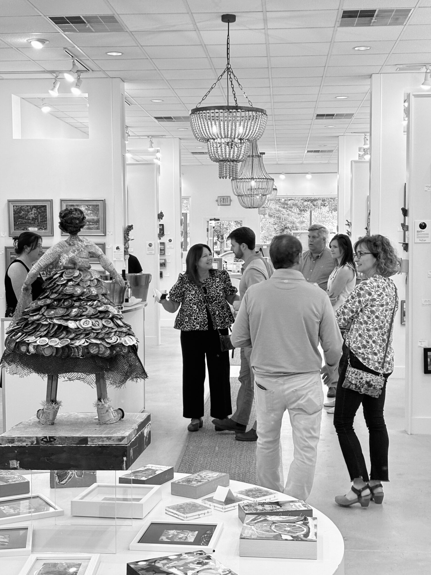 People gather in an art gallery with paintings on white walls and chandeliers hanging from the ceiling.