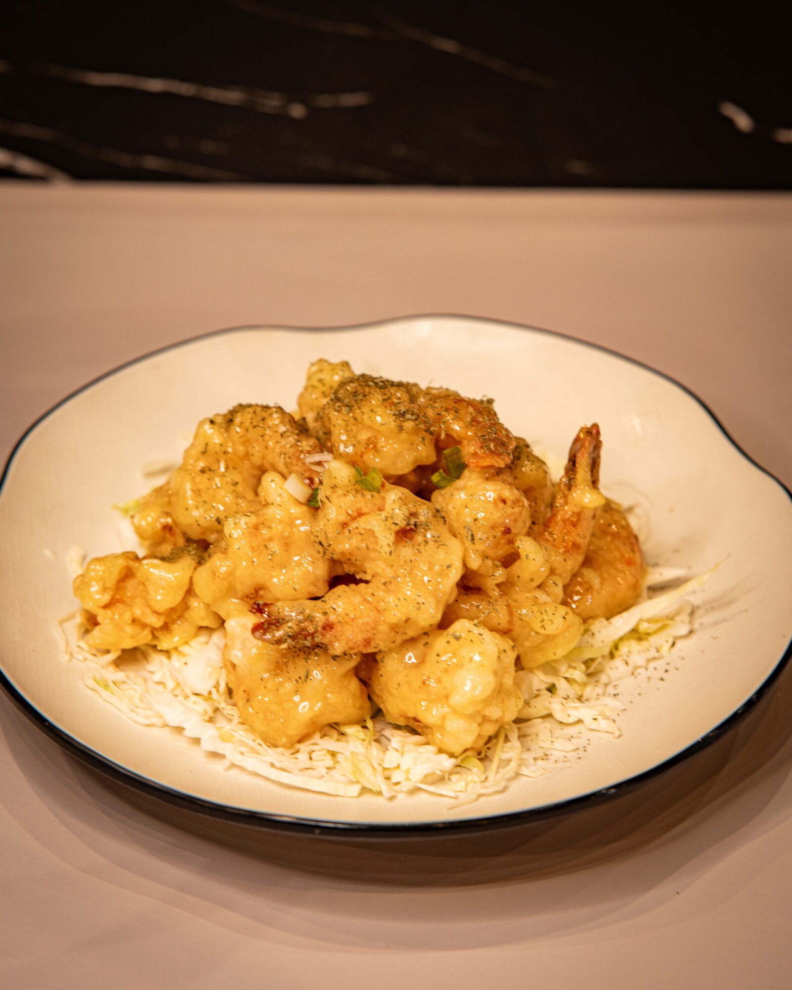 Plate of fried shrimp on a white dish with a black rim, served on a table with a dark background.