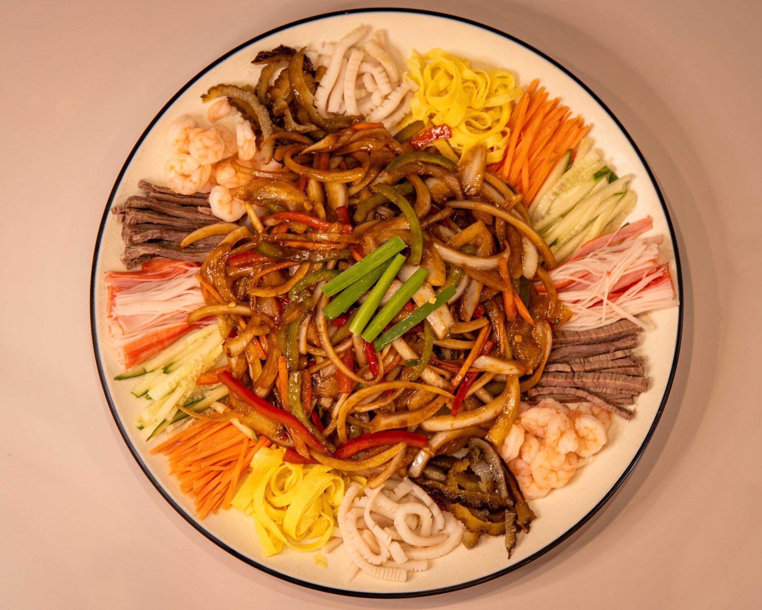 Plate of mixed Asian noodles with vegetables and seafood, arranged around the edge of the plate.