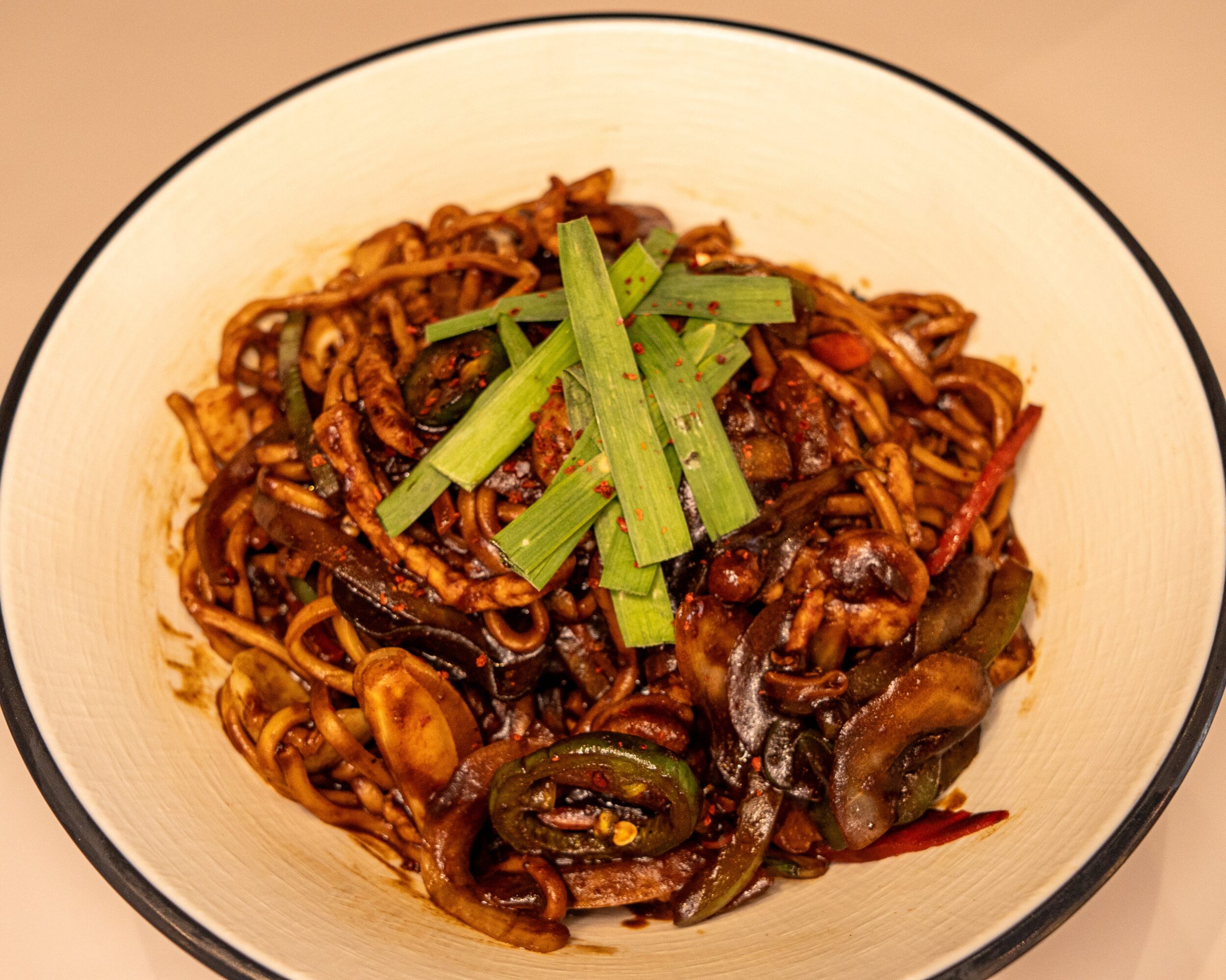 Bowl of stir-fried noodles with vegetables and green onion garnish, viewed from above.