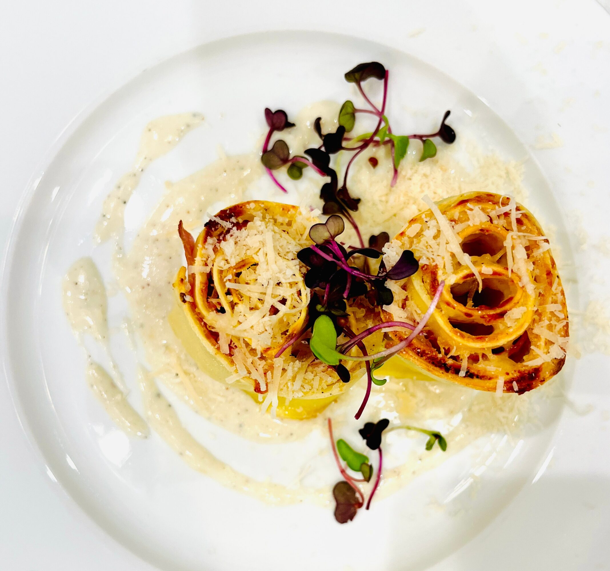 Plate with pasta, garnished with microgreens and cheese, in a creamy sauce, on a white dish.