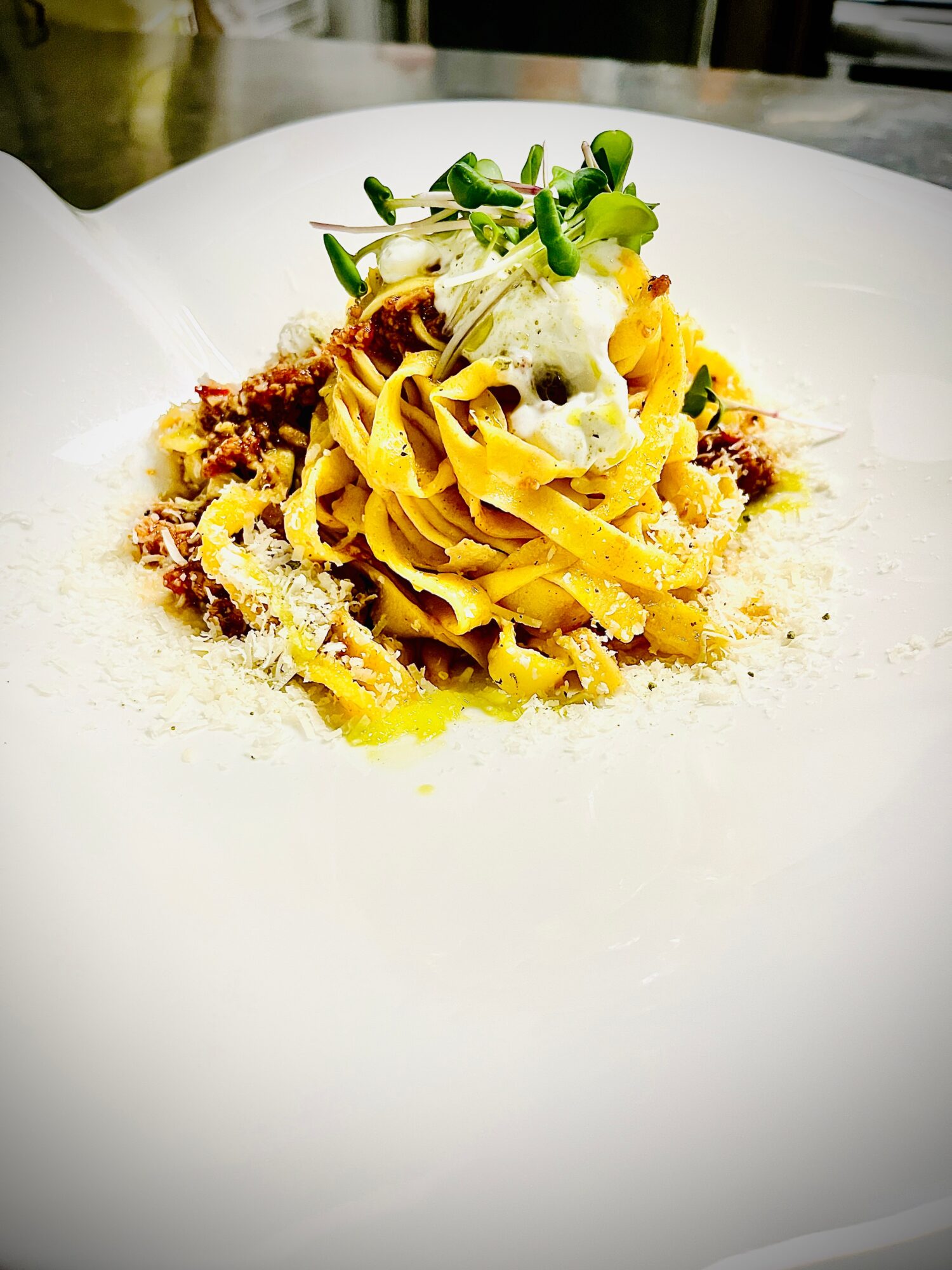 Plate with pasta, topped with a dollop of cream and green garnish, on a white dish.