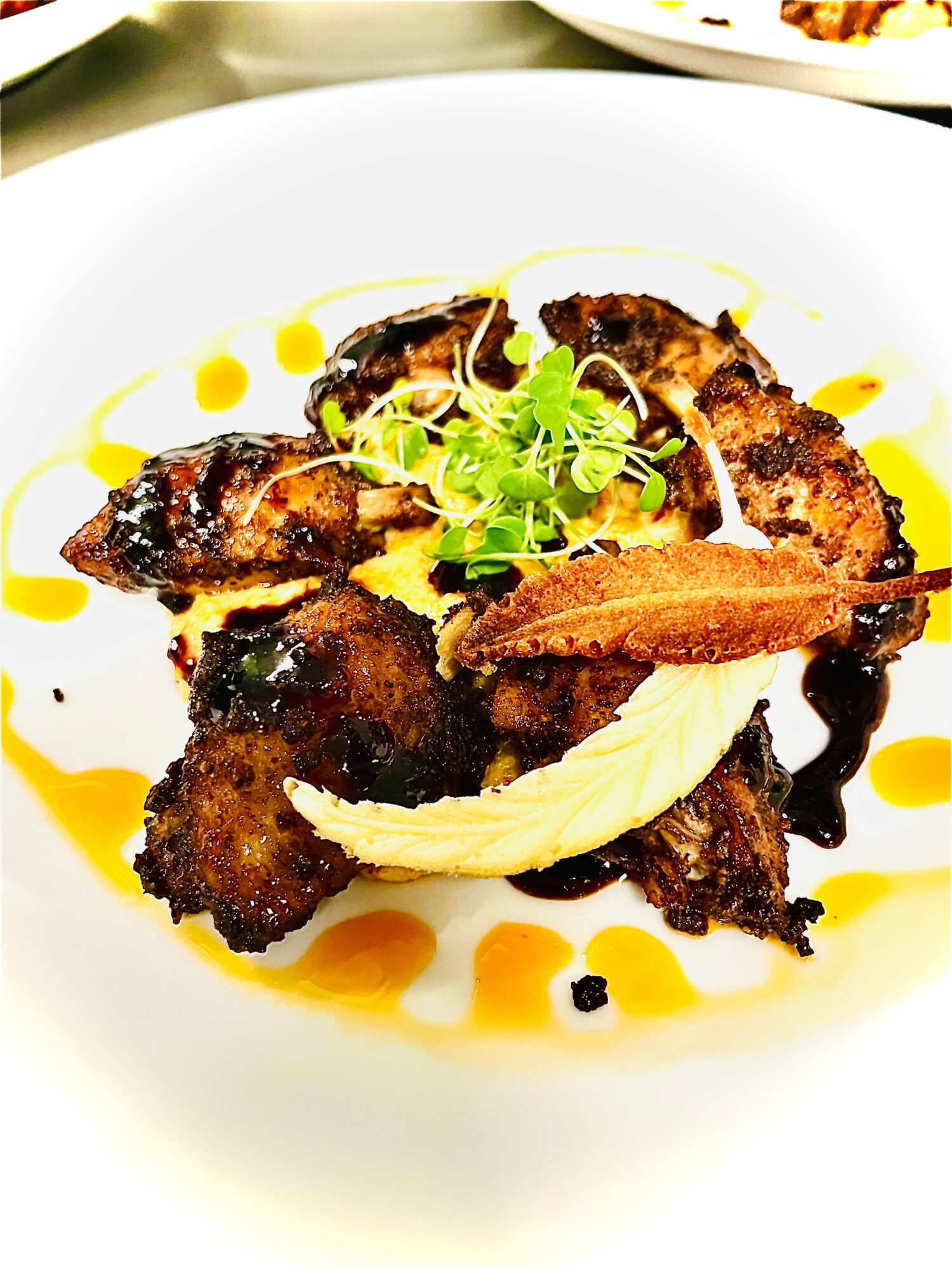 Grilled meat with garnishes and sauce on a white plate, with a blurred background.