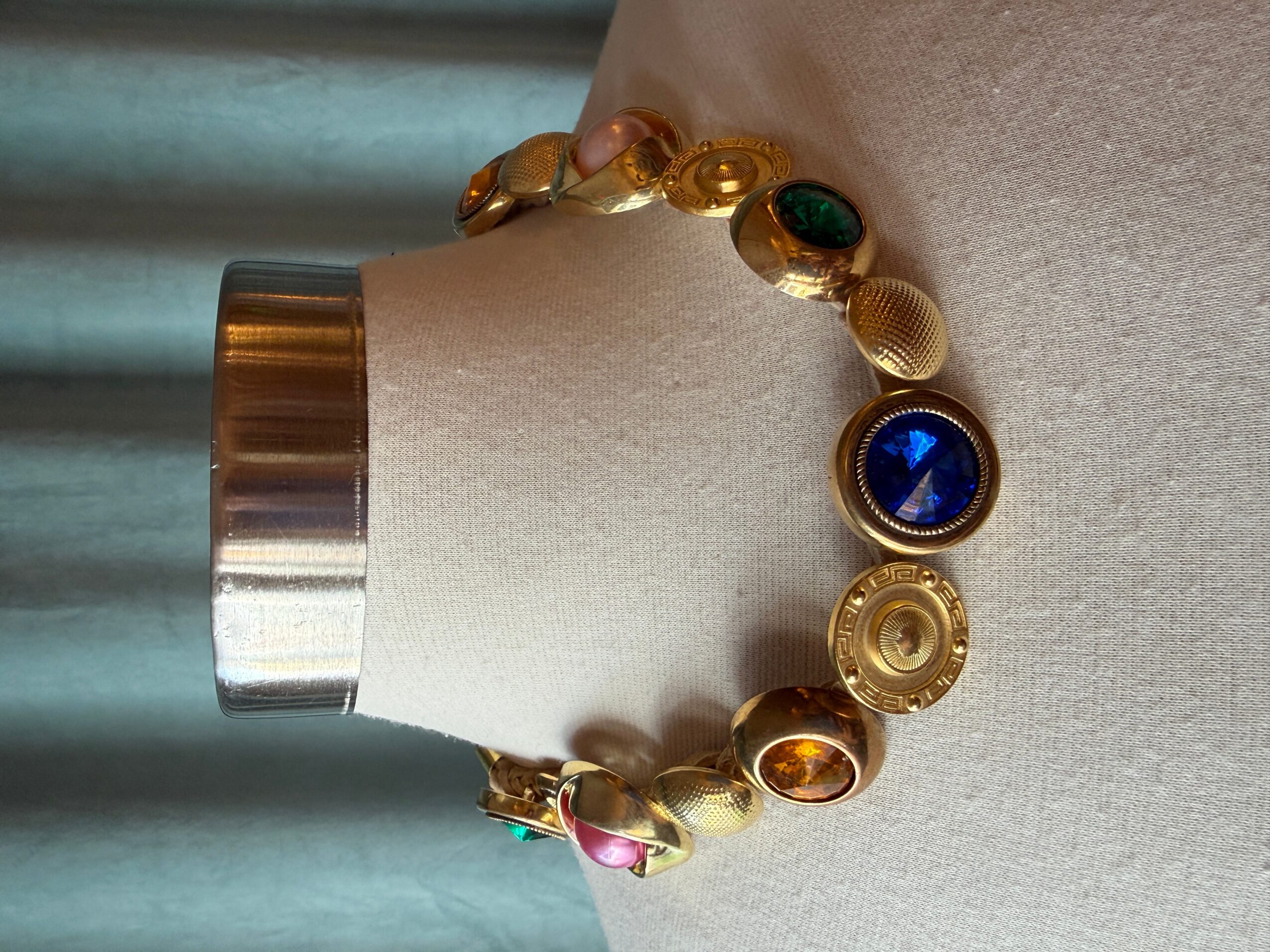 Gold bracelet with colorful circular gemstones on a wrist, against a light background.