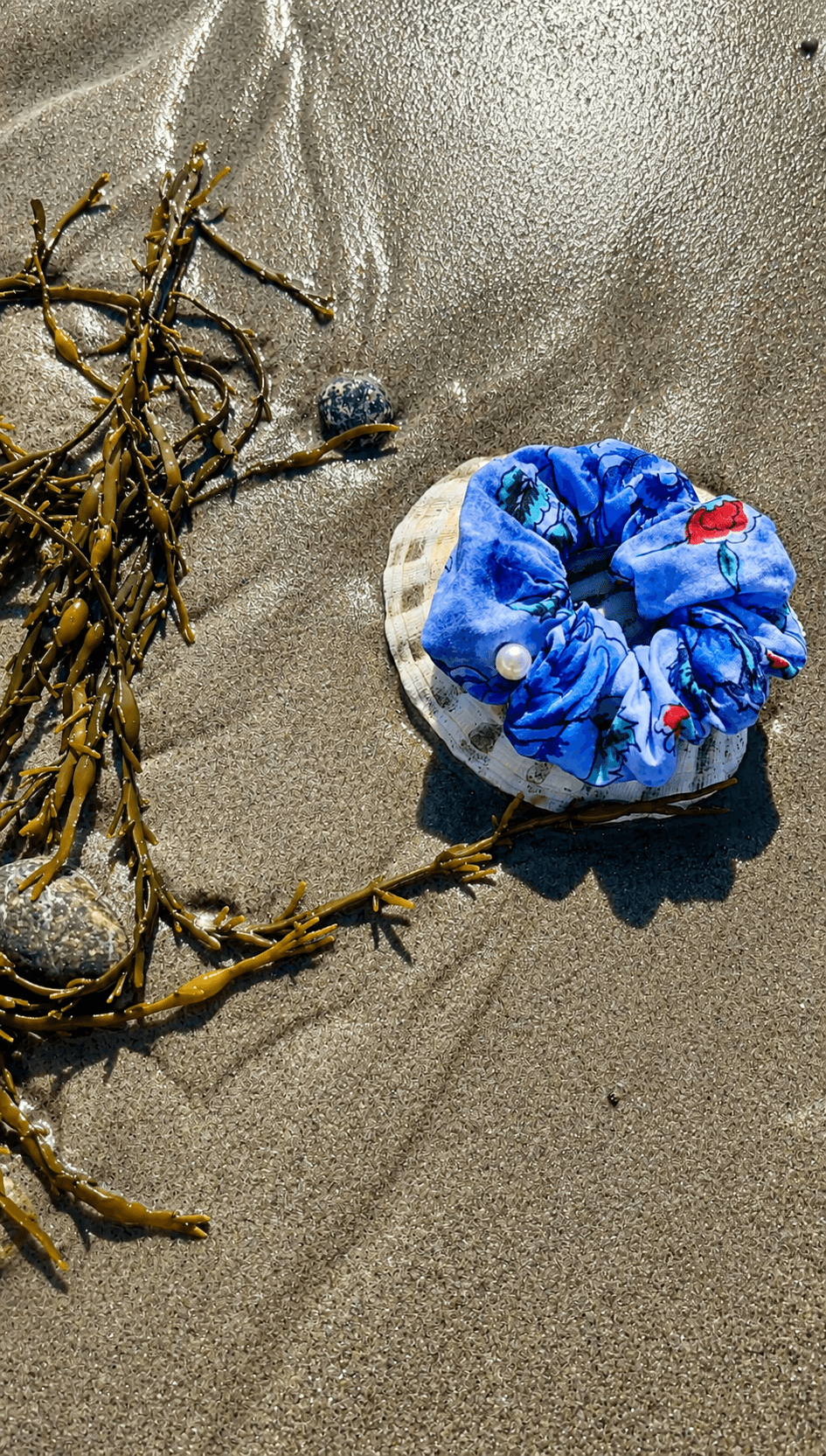 Sand with a blue and white fabric item and dried seaweed, shadows cast on the surface.