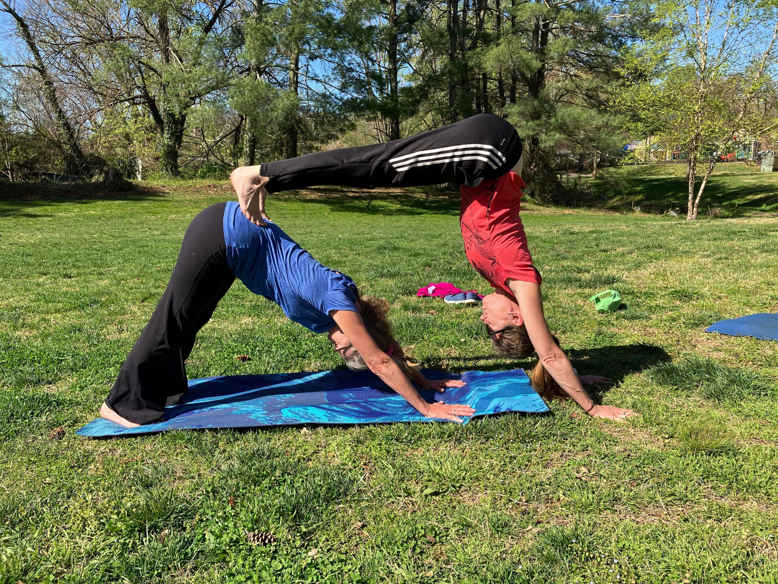Two people practicing acro yoga outdoors on grass, one balancing on hands and feet, the other supporting with legs and hands.