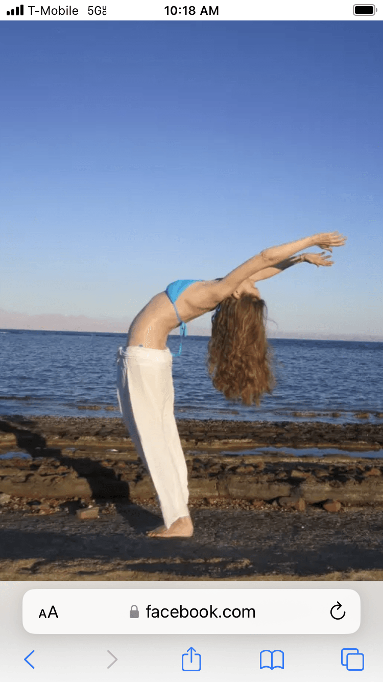 Person performing a backbend on a rocky shoreline with water and sky in the background.
