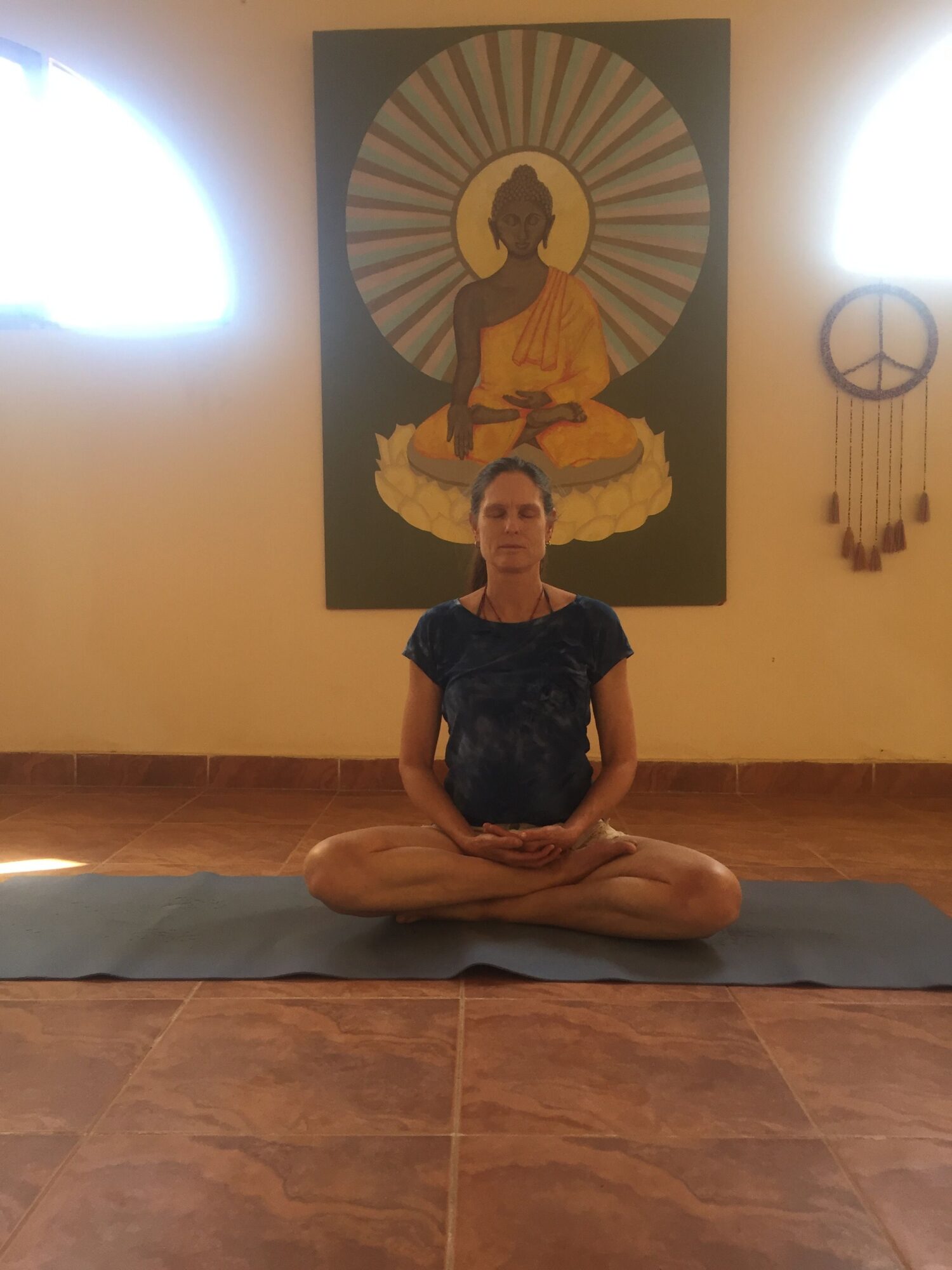 Person sitting cross-legged on a mat in a room with a painting of a woman and a sun in the background.