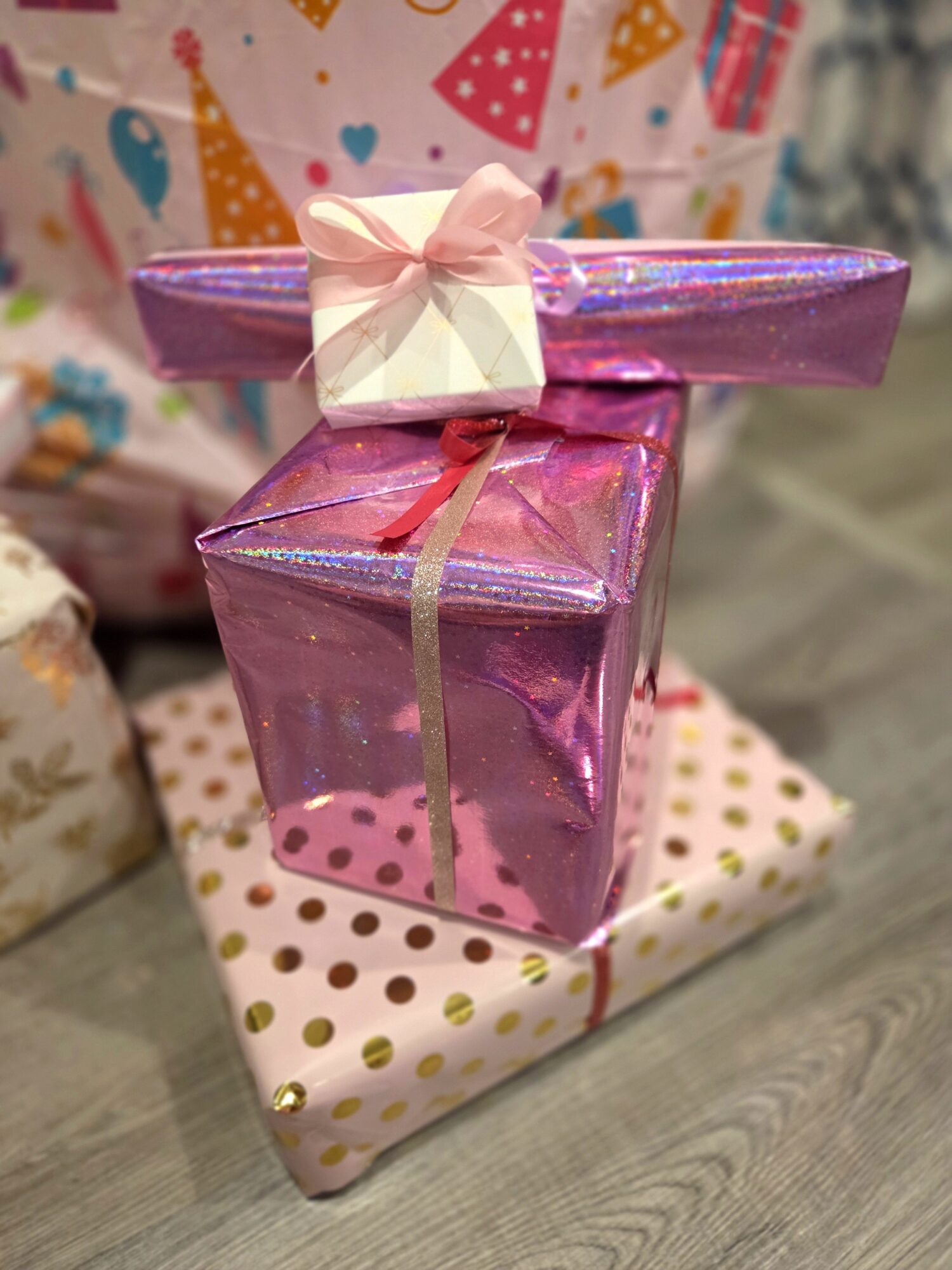 Two wrapped gift boxes, one pink with a ribbon and bow, stacked on a polka dot gift box, on a wooden surface.