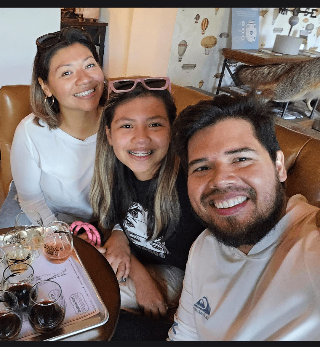 Three people smiling at a table with wine glasses, in a cozy indoor setting.