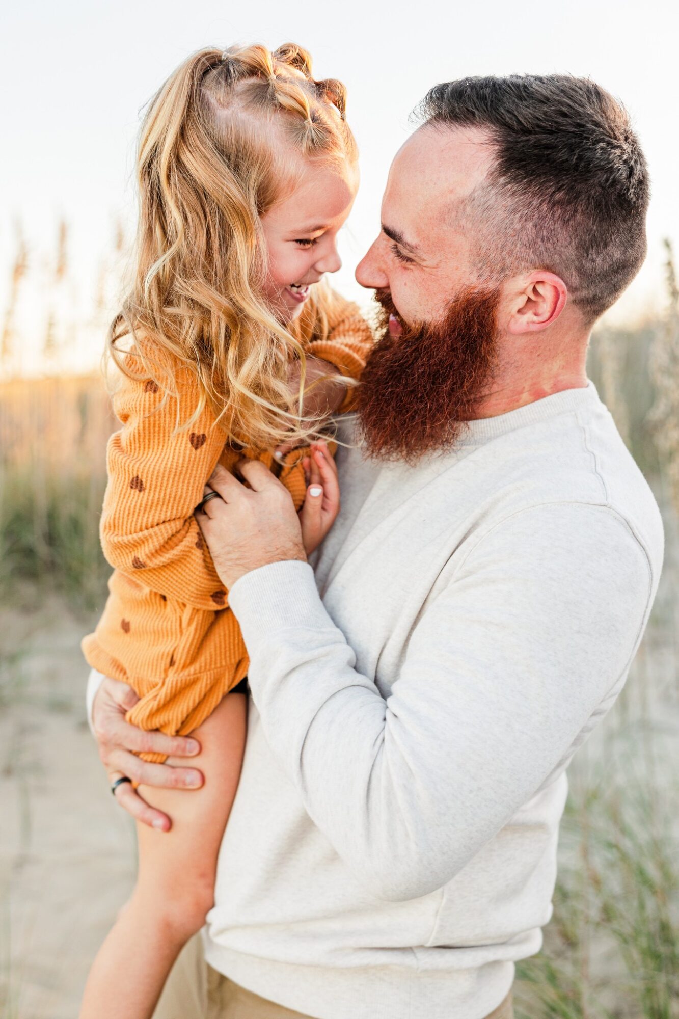 A man and a young girl are smiling and touching foreheads outdoors, with a blurred natural background.