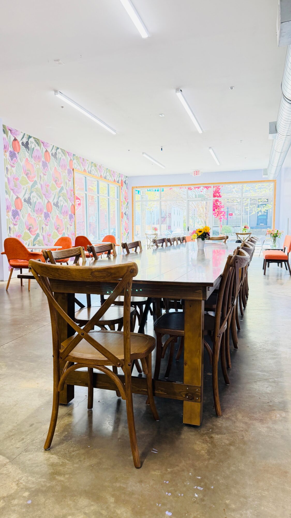 Long table with chairs in a room with colorful wall art and large windows, bright lighting, and concrete floor.
